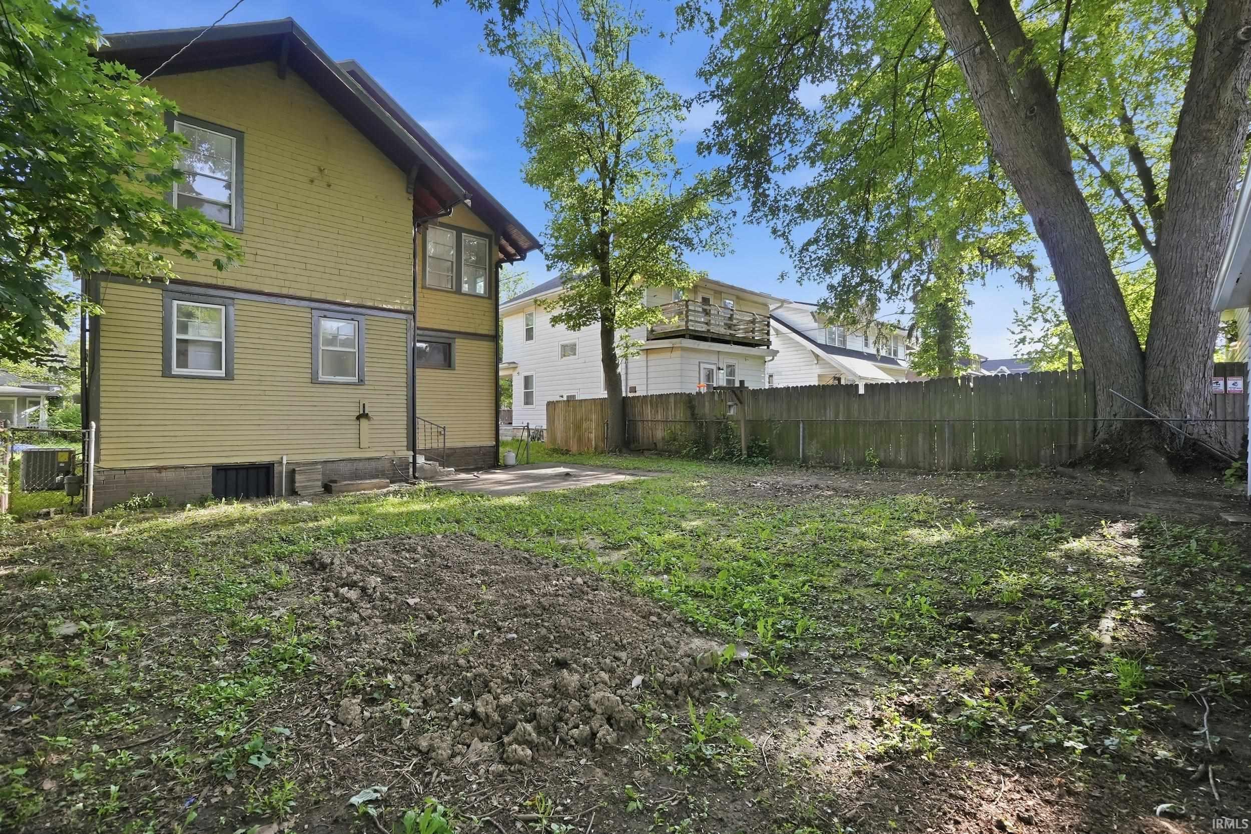 Spacious backyard offering a large, open grassy area, surrounded by mature trees, and featuring a wood privacy fence