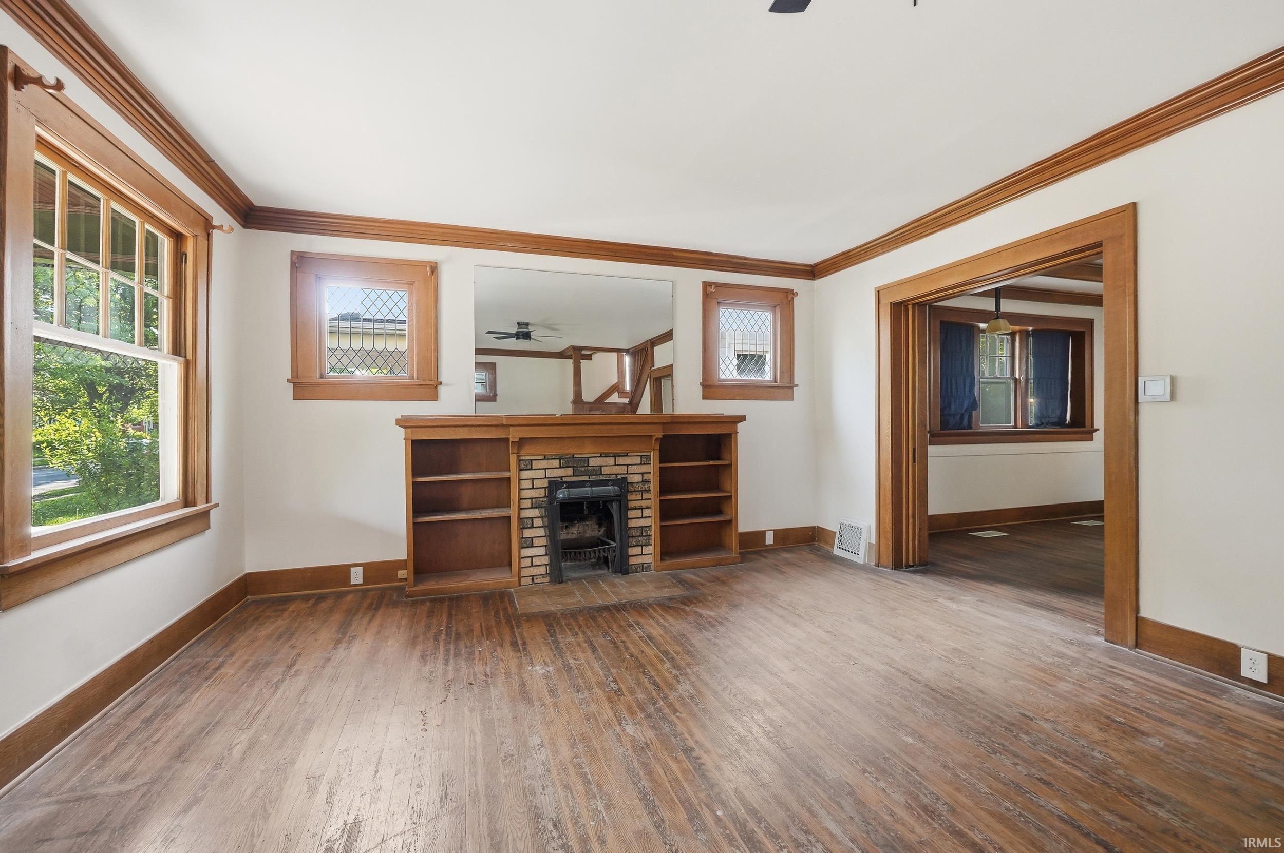 Living area featuring wood-finish flooring, a brick fireplace with built-in shelving, and wood trim detailing