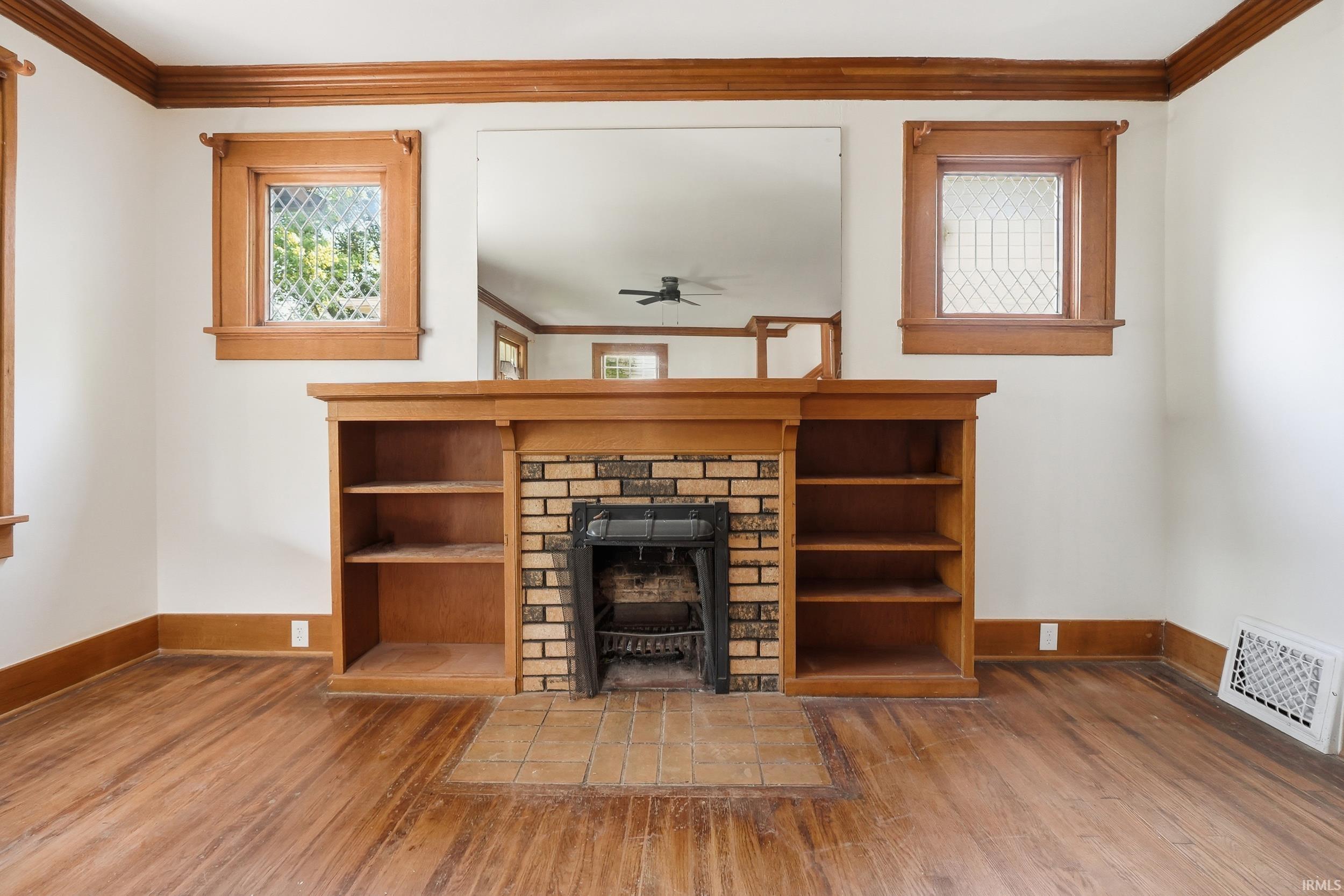 Fireplace hearth with brick surround and integrated built-in shelving, featuring wood-finish flooring, wood trim, and leaded glass windows