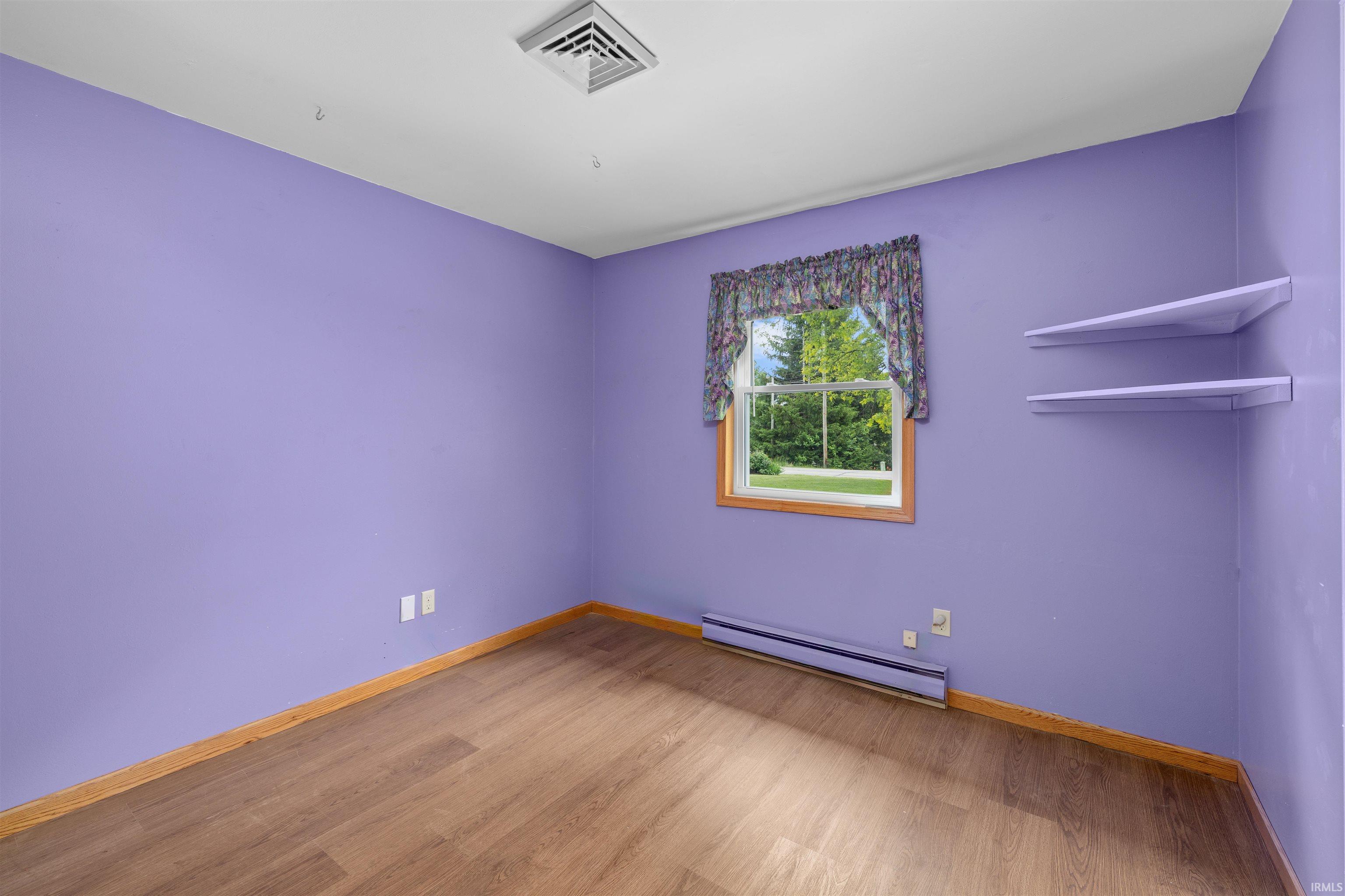 Interior space featuring wood-finish flooring, a window with wood trim, and a baseboard heating unit