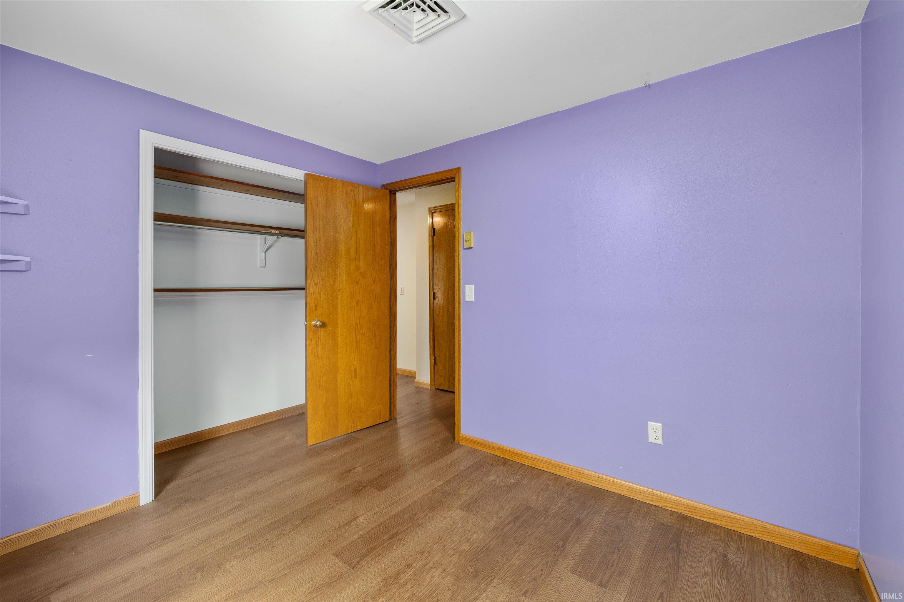 Interior room with wood-finish flooring, a built-in closet with shelving and hanging rods, a solid wood door, and baseboard trim