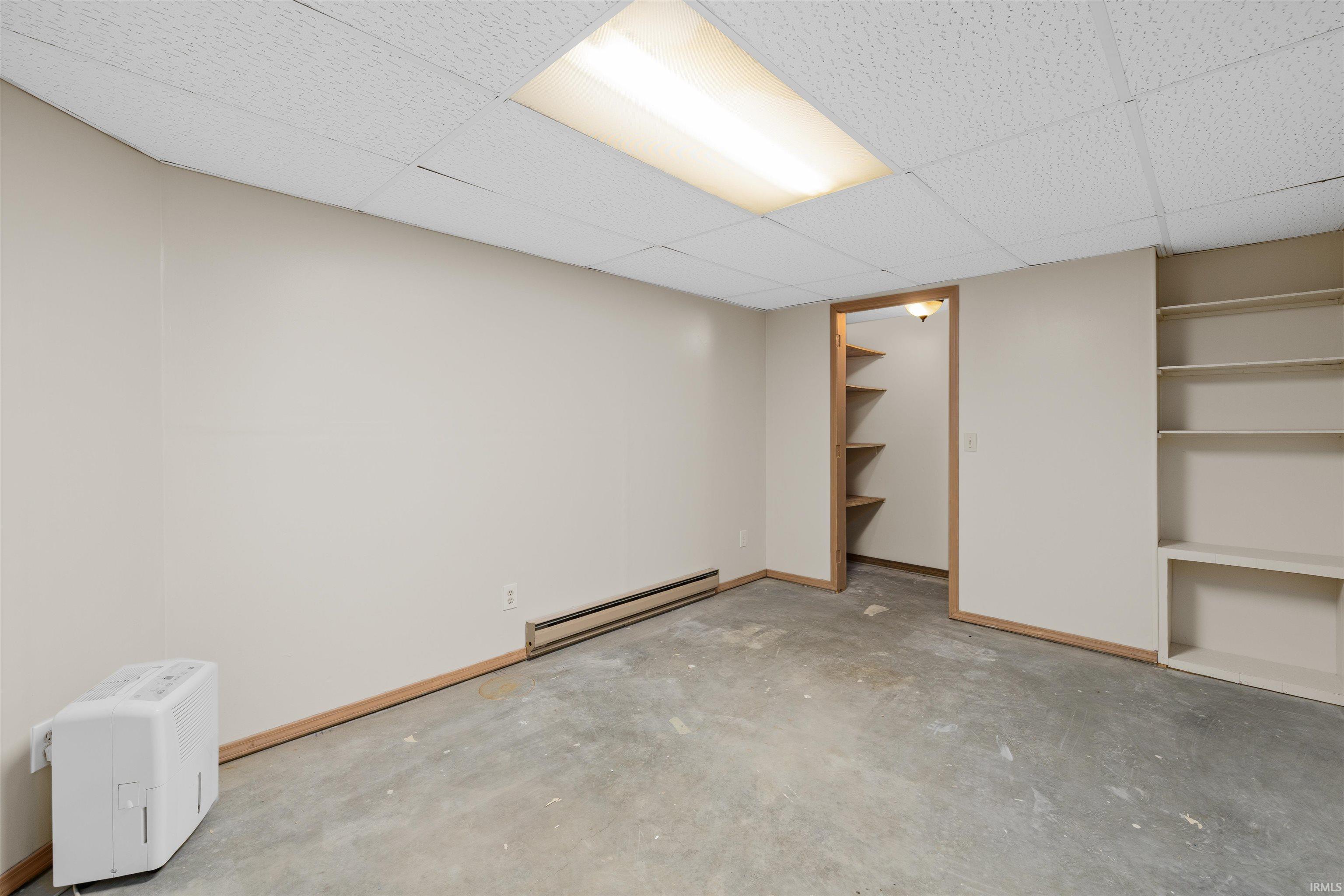 Unfinished lower level space featuring exposed concrete flooring, a drop ceiling with recessed lighting, and baseboard heating
