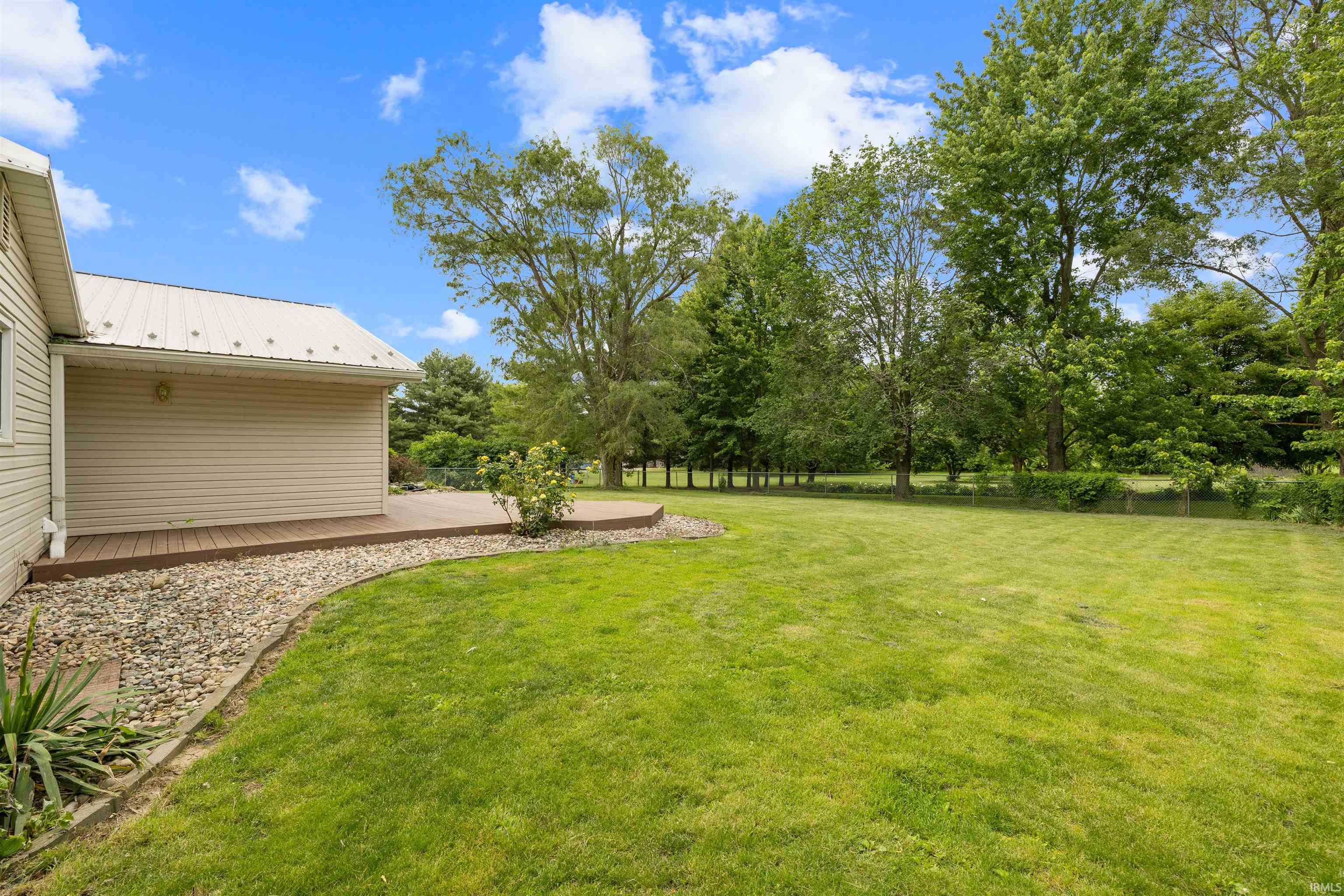 Expansive backyard featuring a curved composite deck, stone landscaping border, and mature perimeter trees