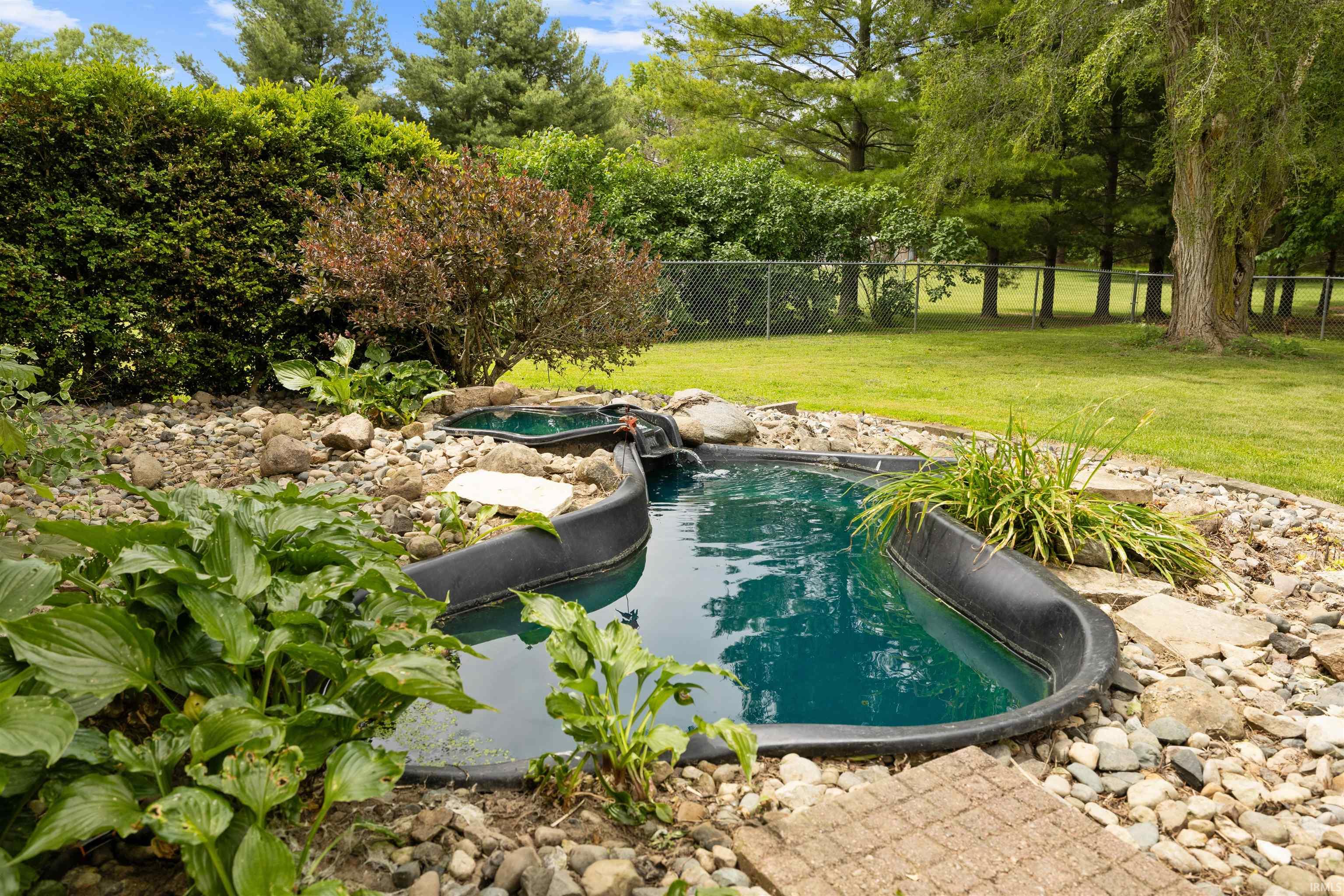 Tiered water feature surrounded by decorative river rock, lush foliage, and mature trees