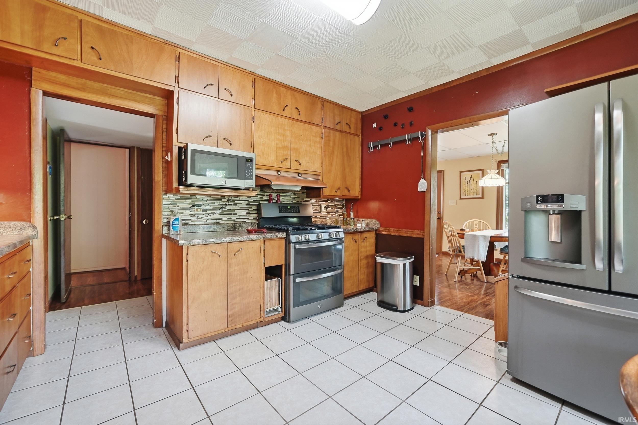 Kitchen featuring wood cabinetry, white tiled flooring, a stainless steel double oven range, stainless steel refrigerator, and a tiled backsplash