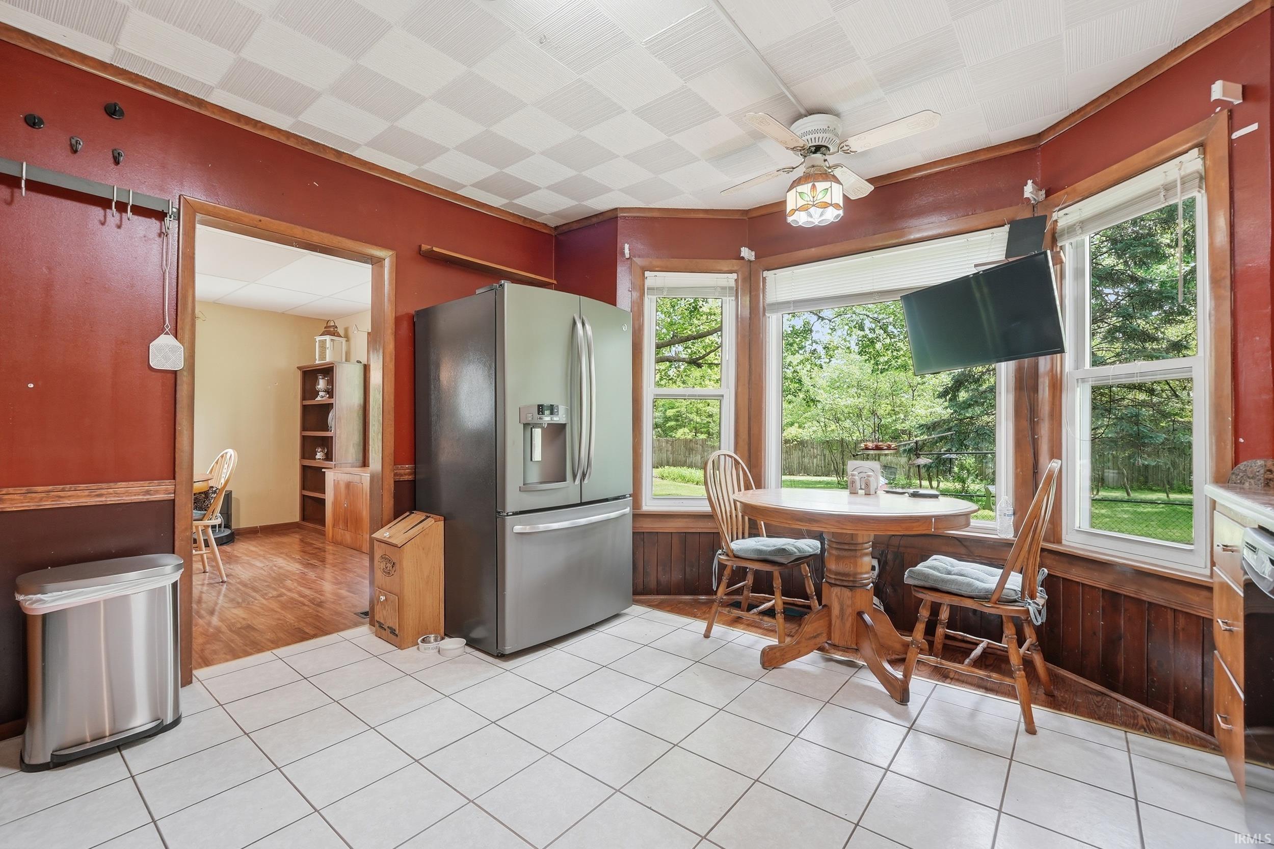 Kitchen featuring white square tile flooring, stainless steel French door refrigerator, red walls with wood paneling, bay window, and ceiling fan