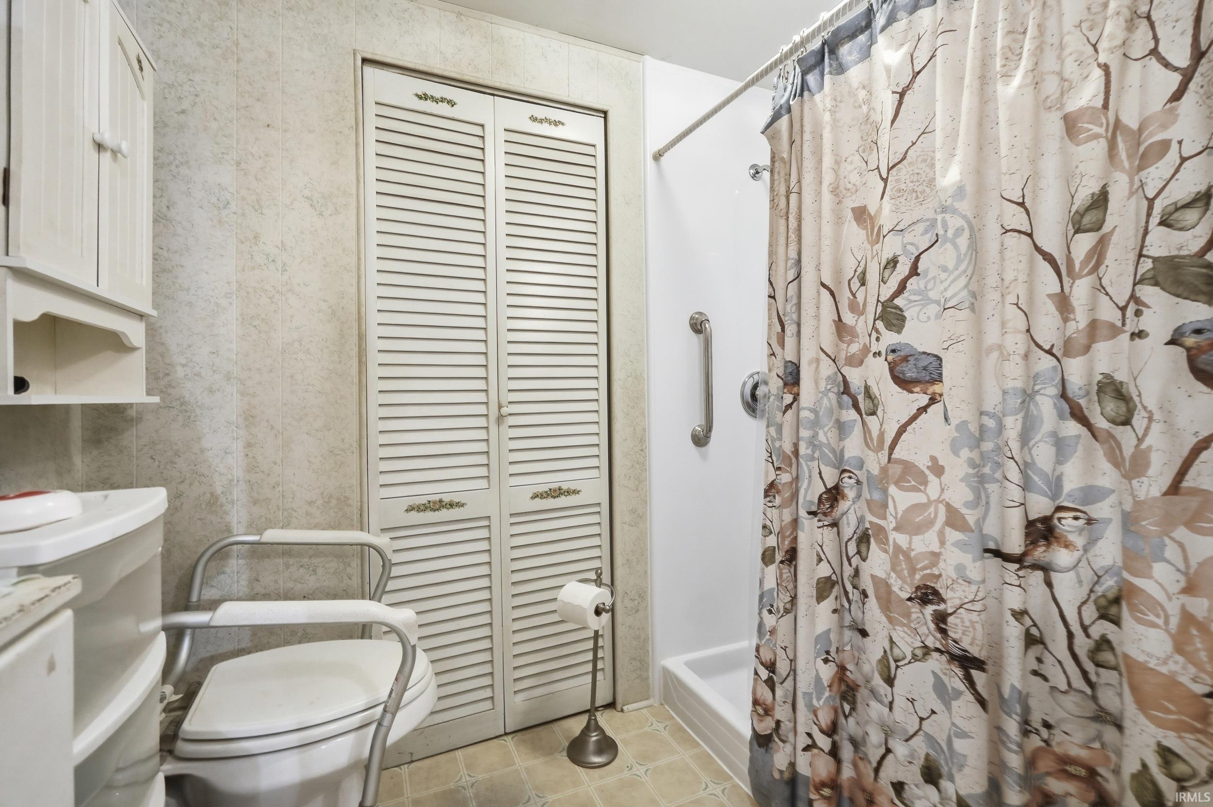 Bathroom with a walk-in shower featuring a grab bar, white vanity, and louvered bi-fold doors