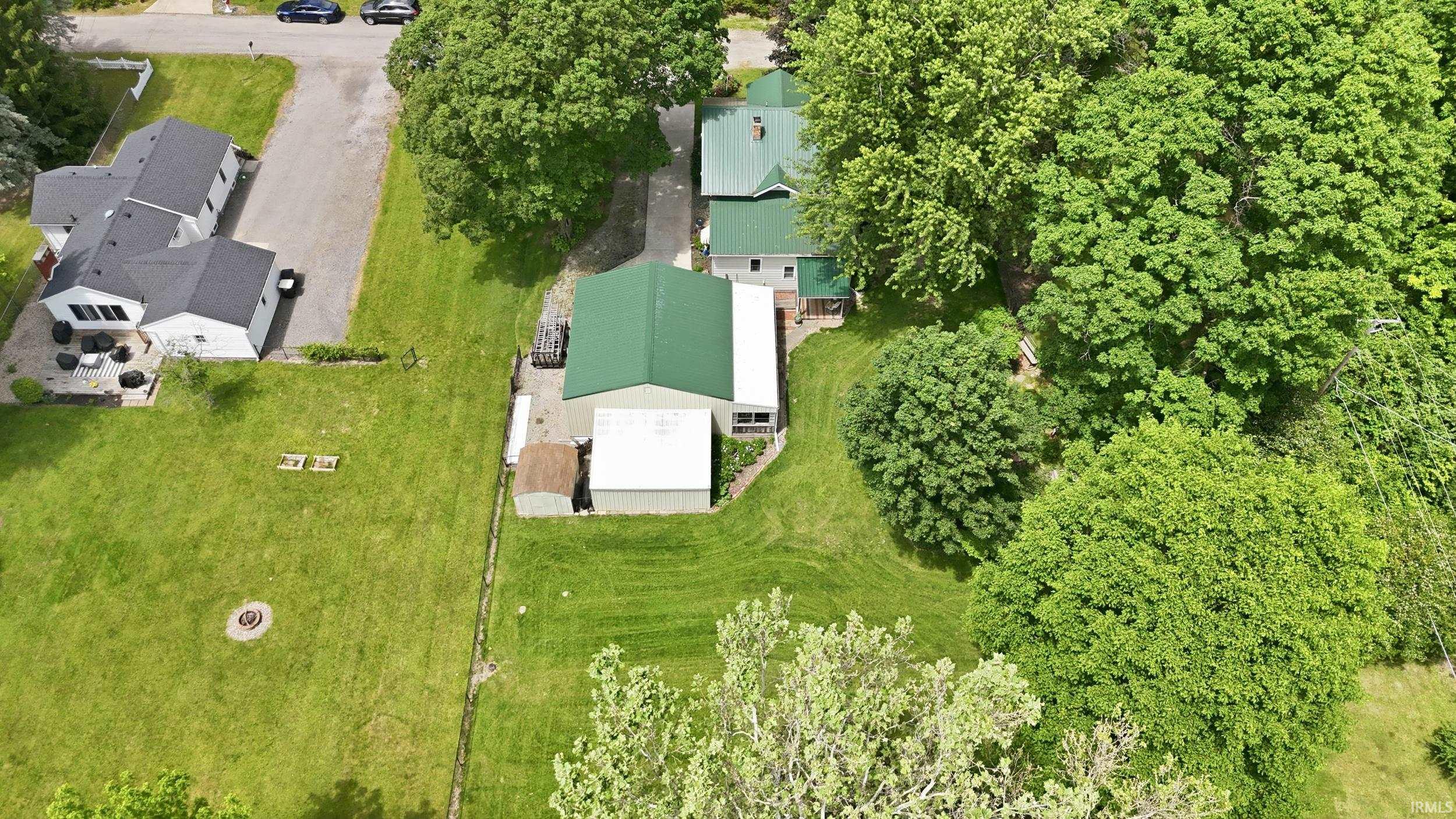 Expansive green lot featuring multiple structures, mature trees, and a fire pit