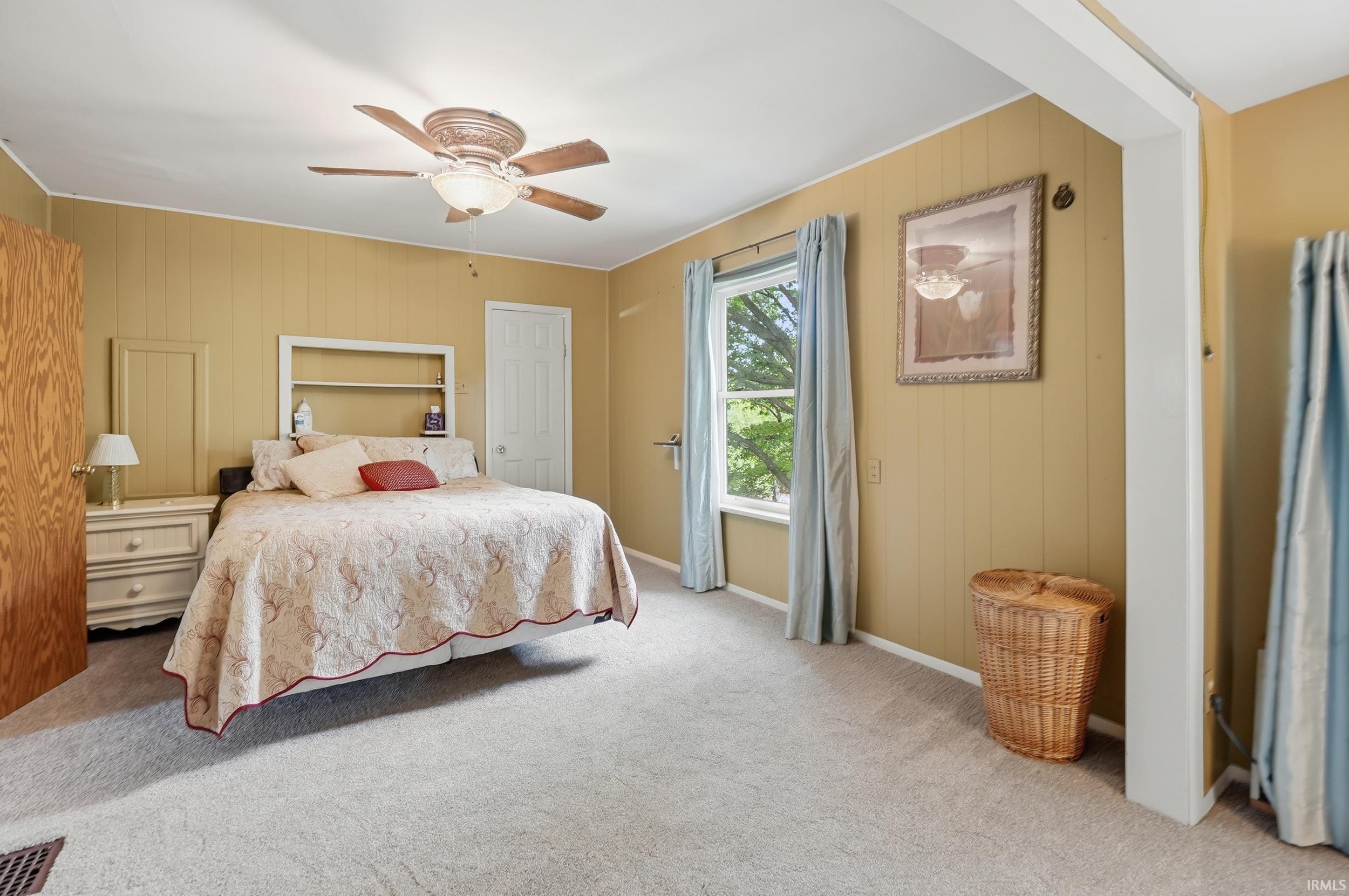 Carpeted room featuring a ceiling fan with integrated lighting, a built-in headboard shelf, and a window with light blue drapes