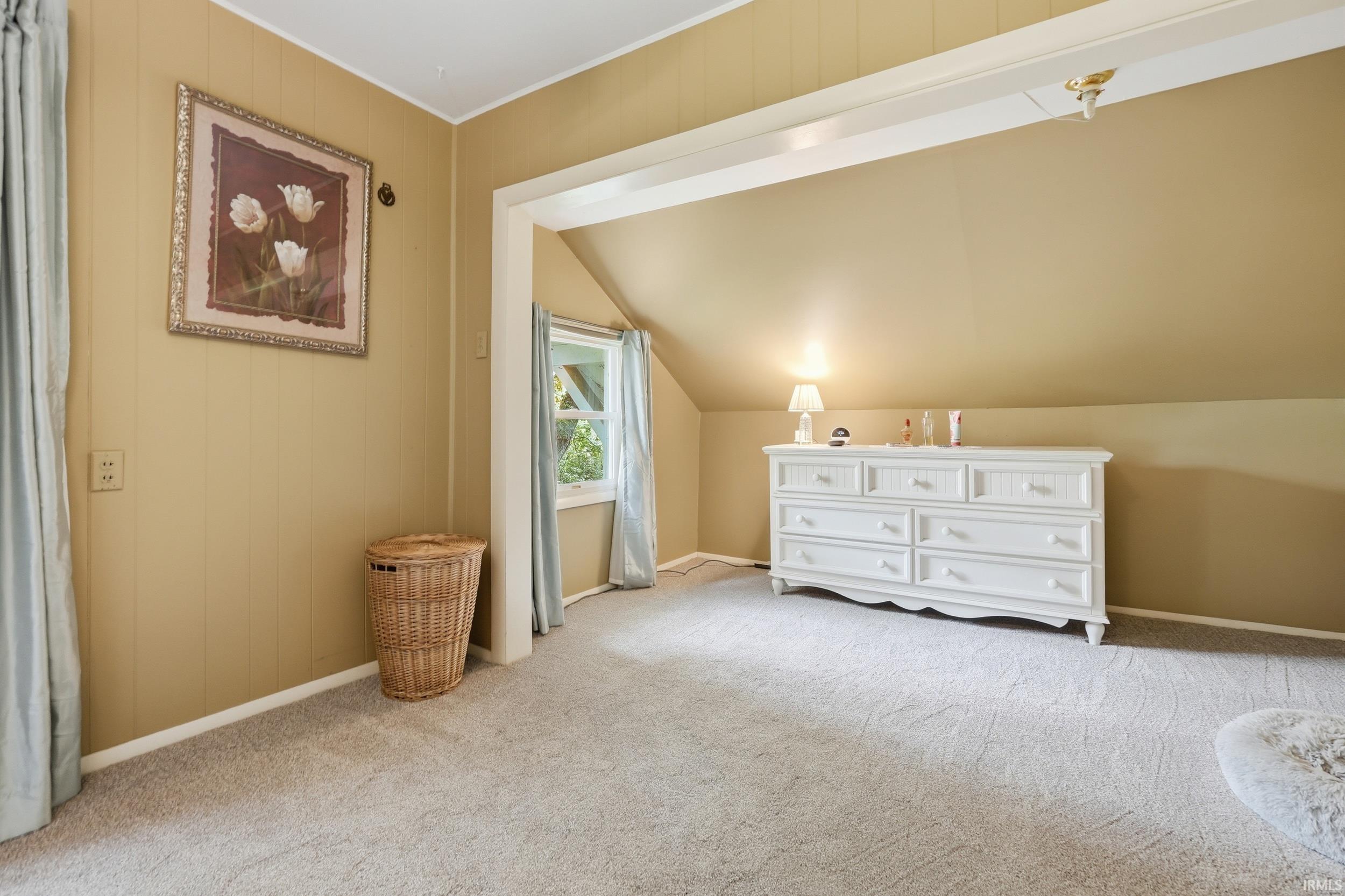 Carpeted room featuring a window with natural light, sloped ceilings, and wood-paneled walls