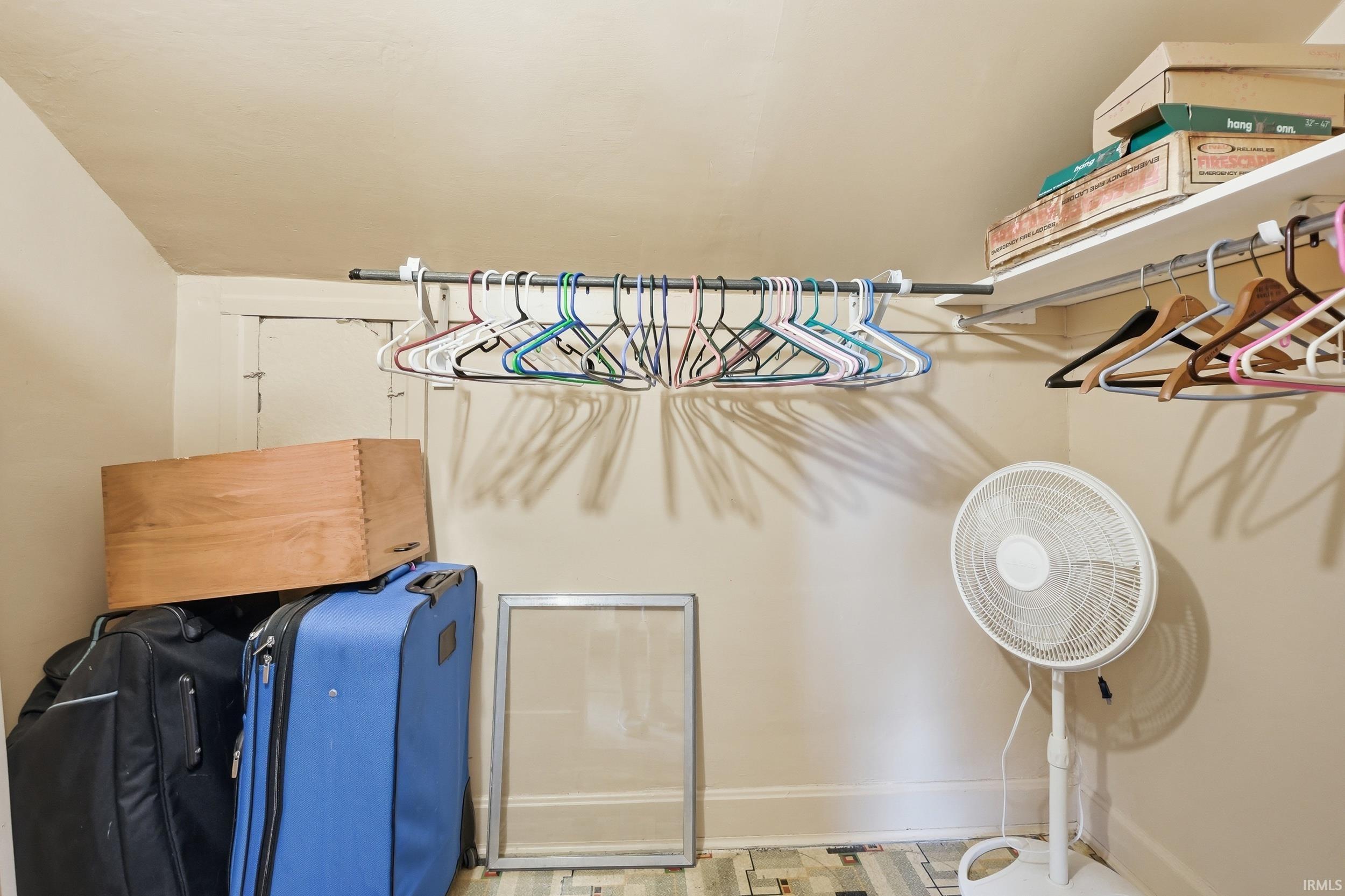 Sloped ceiling storage space featuring a built-in hanging rod and overhead shelving
