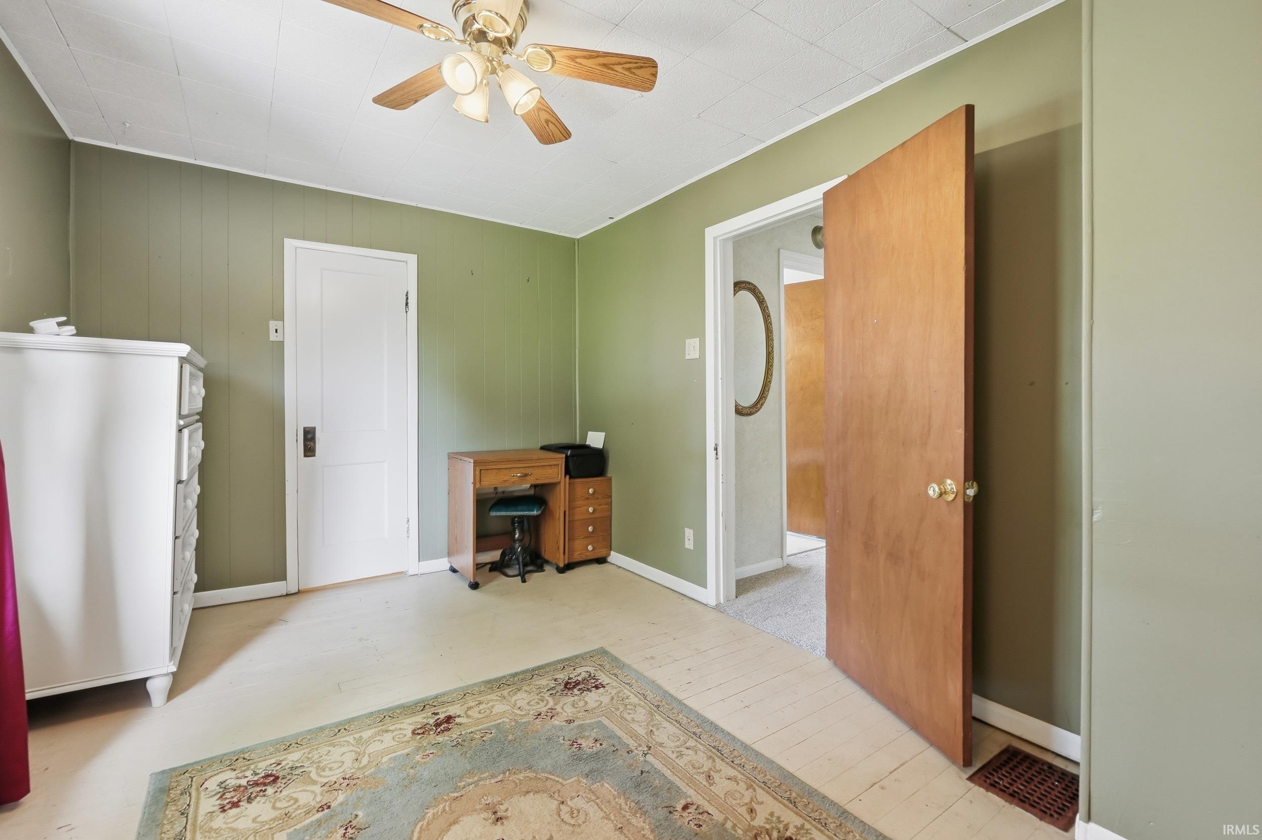 Room featuring a ceiling fan, light green wall paneling, and a light-colored flooring