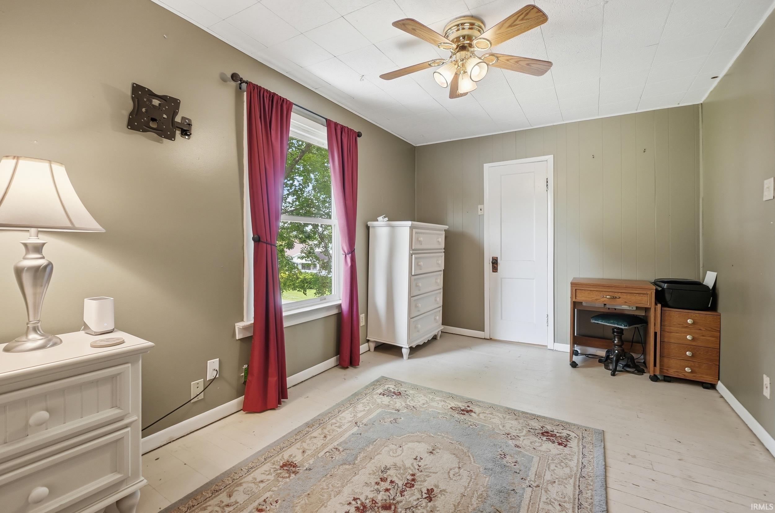 Interior room featuring light-toned flooring, textured wall paneling, a ceiling fan with integrated lighting, and a white paneled door