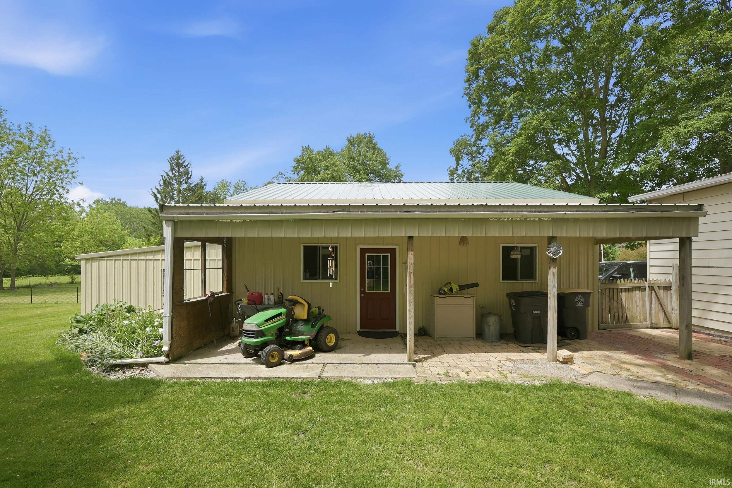 Spacious utility building featuring a covered porch, metal roof, and an attached carport with brick-patterned paving