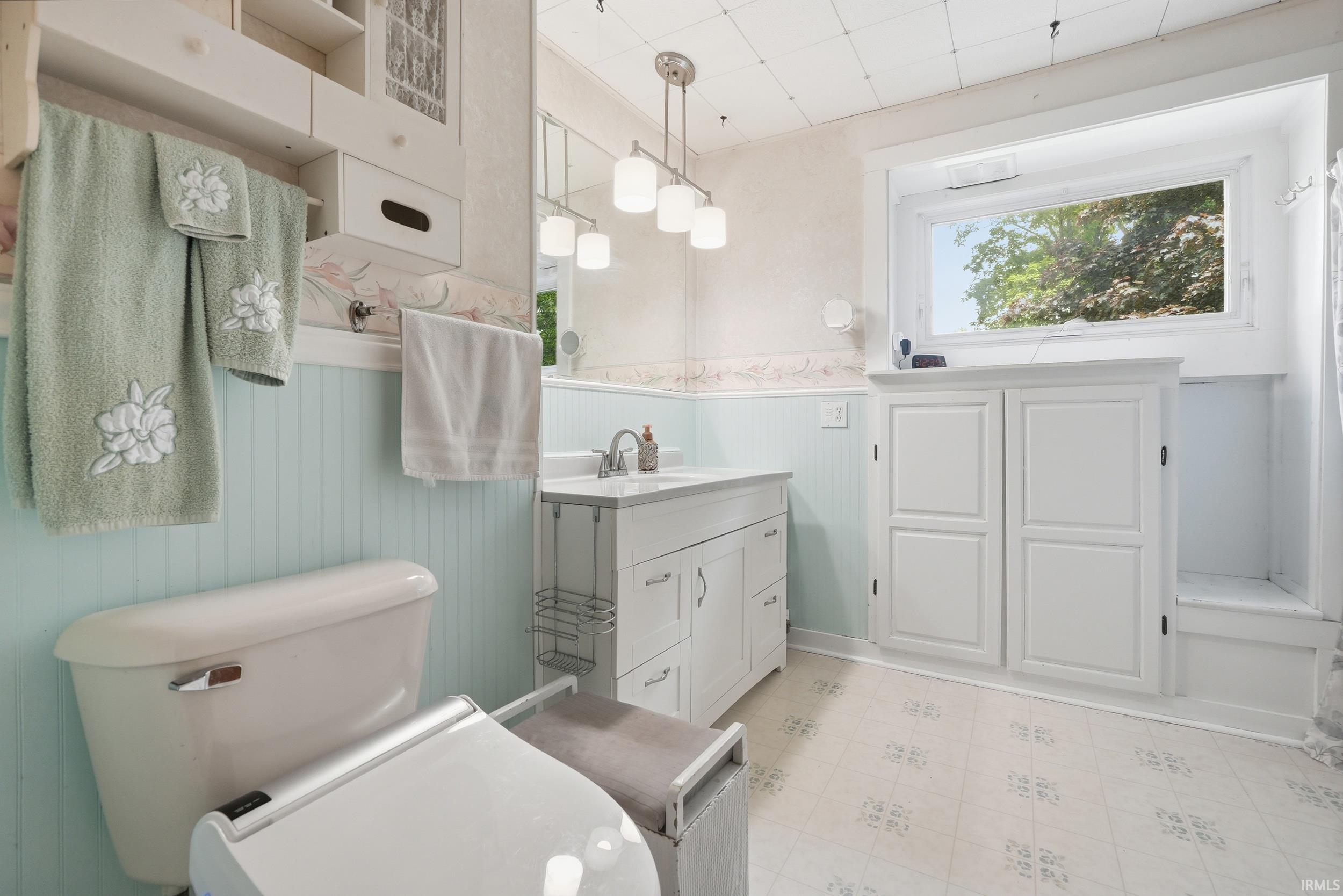 Light-filled bathroom featuring beadboard wainscoting, white vanity with integrated sink, white storage cabinetry, and a window with natural light