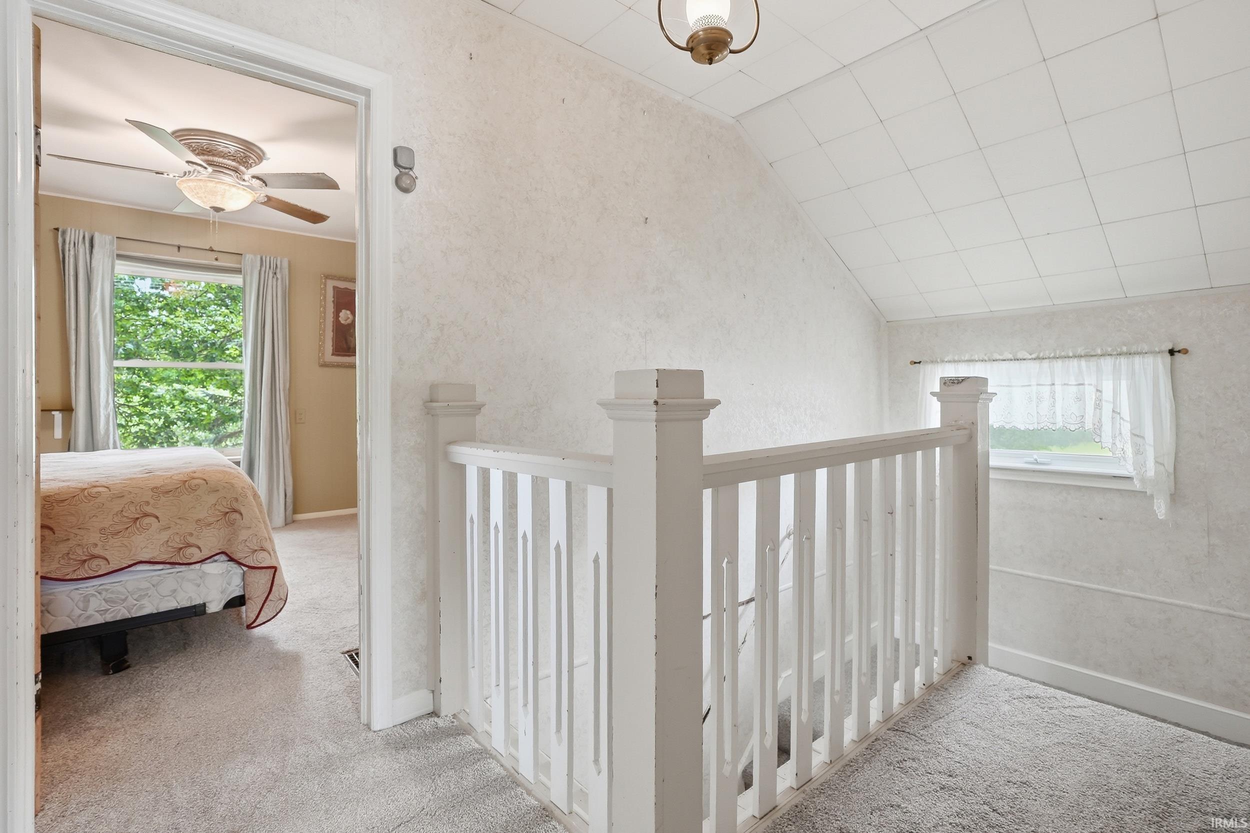 Upper-level landing featuring a white wooden balustrade, textured walls, and a window providing natural light