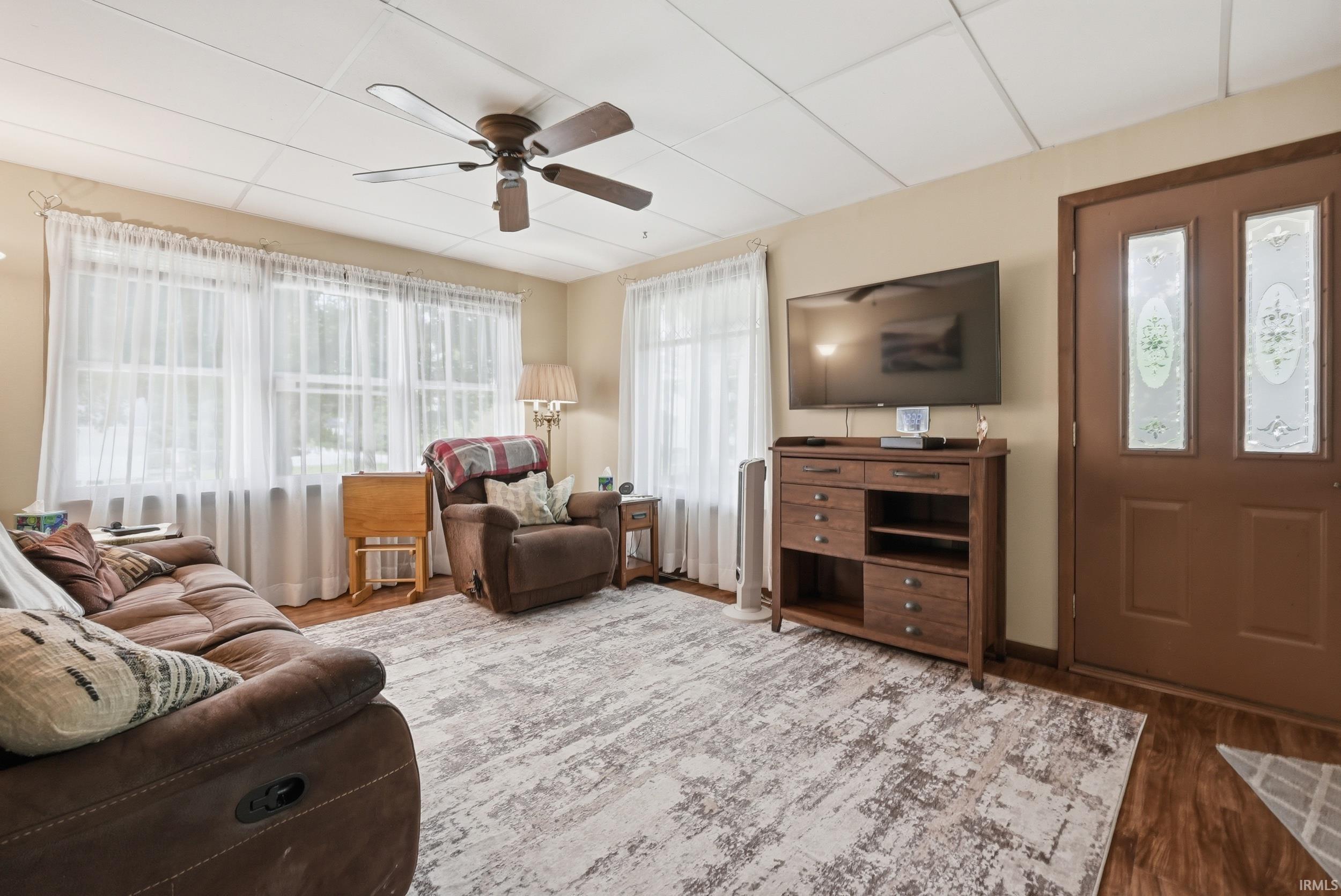 Living area featuring wood-finish flooring, a decorative entry door with frosted glass panels, and a ceiling fan with integrated lighting