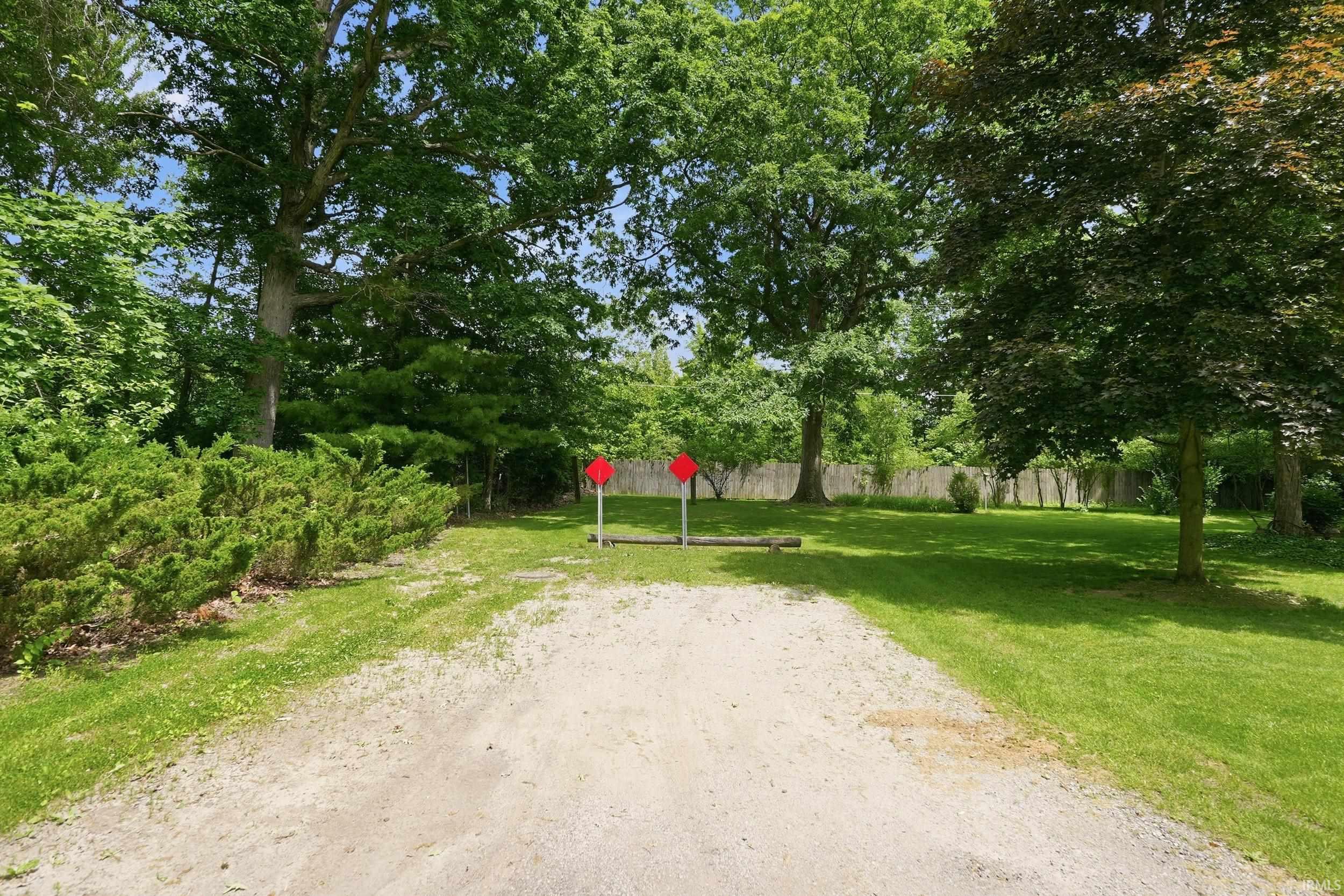 Spacious outdoor area featuring a gravel path, expansive lawn, mature trees, and established perimeter shrubbery