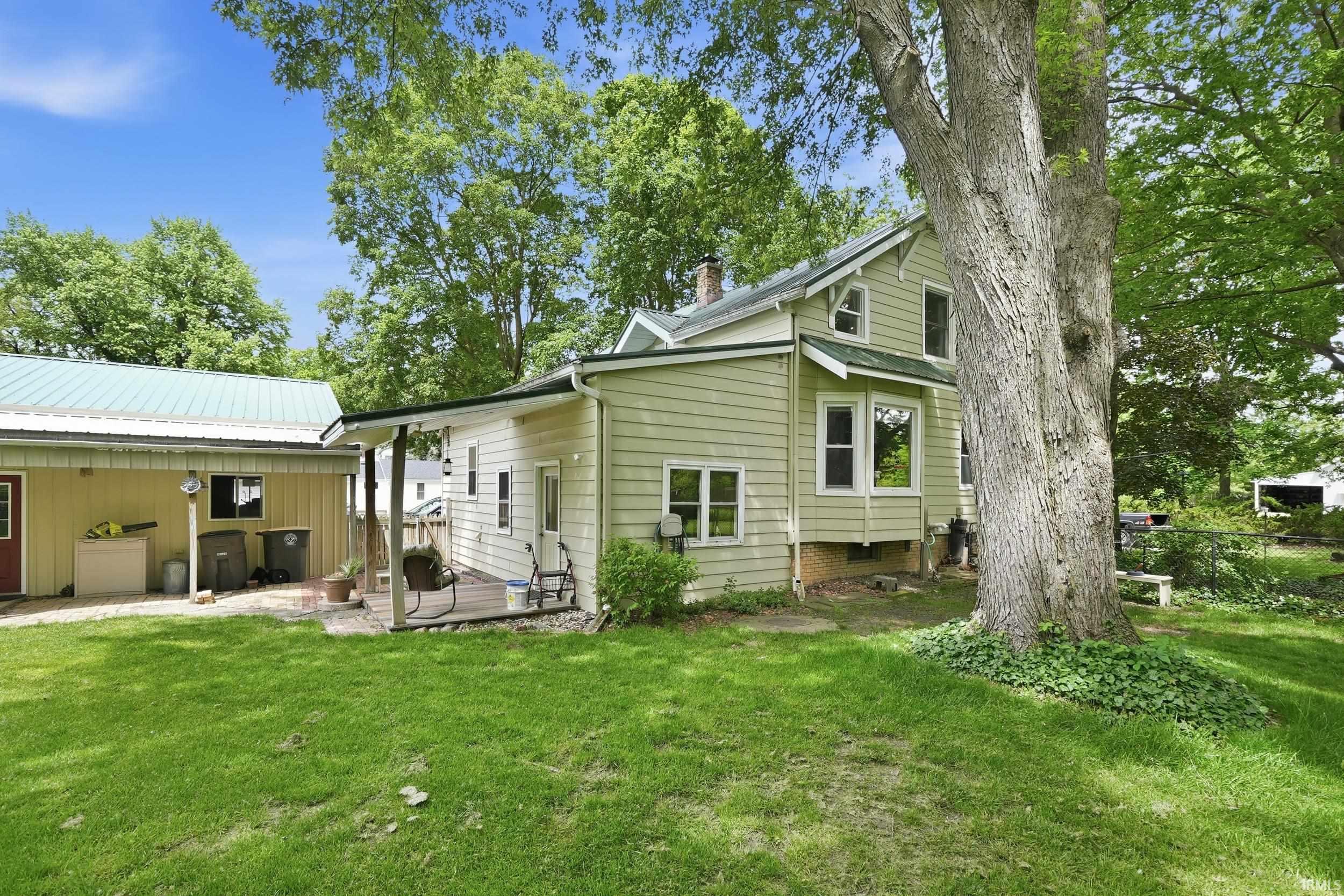 Expansive green lawn featuring a large mature tree, a covered porch, and an attached auxiliary building with a metal roof