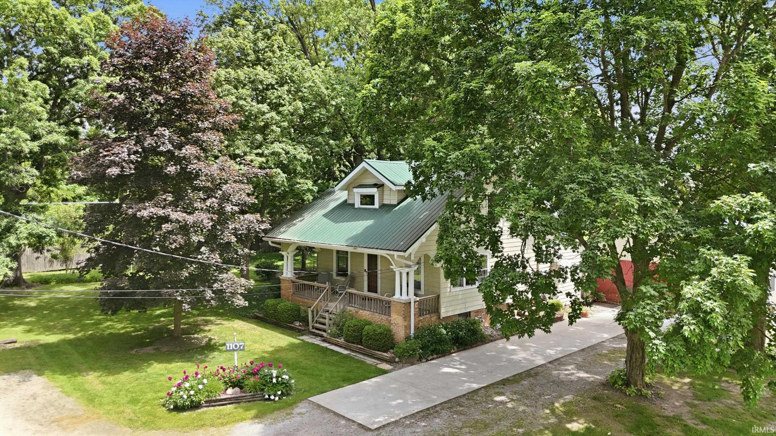Gable-style residence featuring a green metal roof, light-colored siding, and a covered front porch with white columns