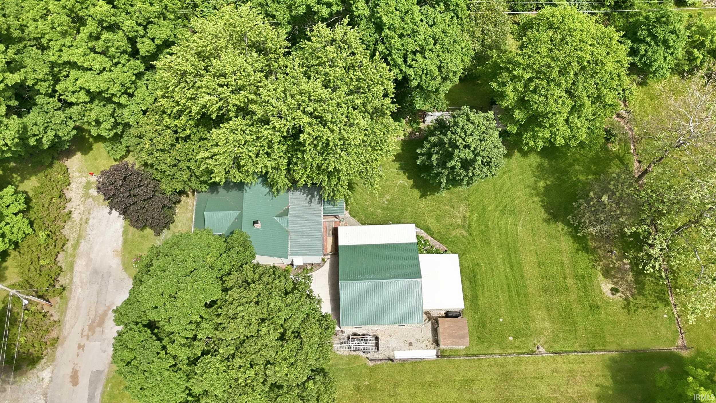 Expansive property featuring a residence with a green roof, a large detached outbuilding with a green roof, a substantial grassy area, mature trees, and a gravel drive