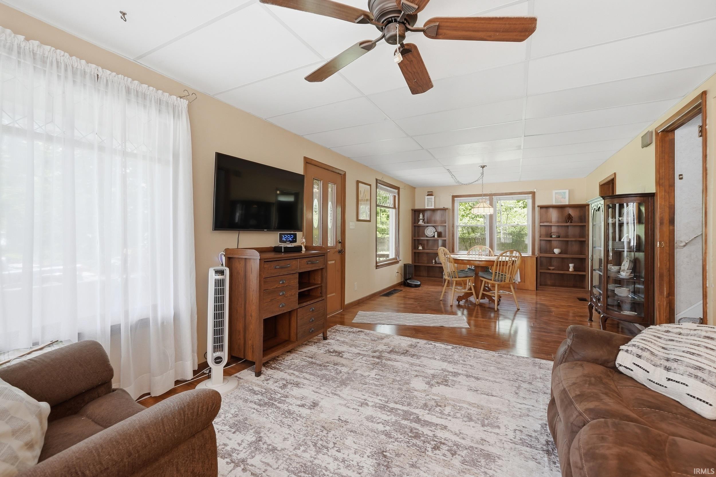 Open concept living and dining area featuring wood-finish flooring, a ceiling fan, and multiple windows
