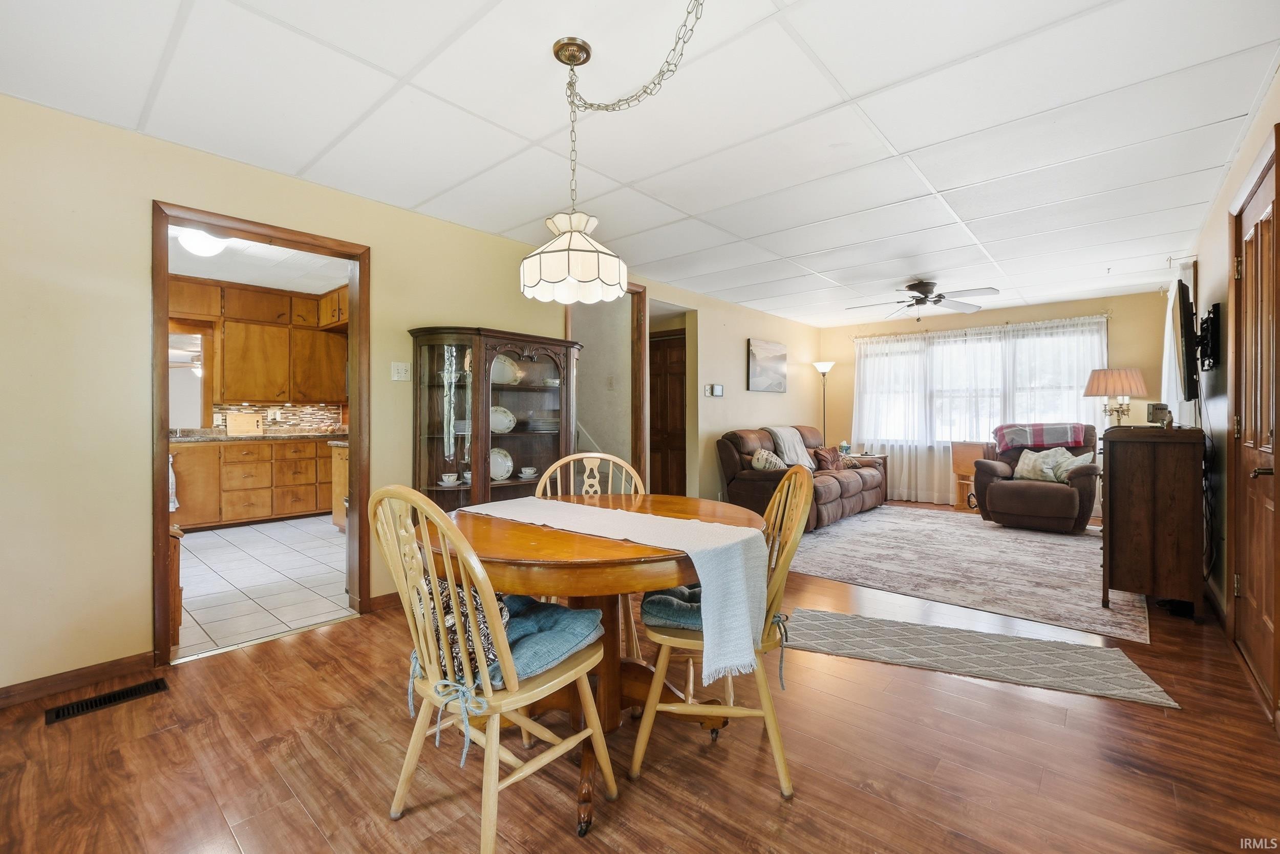 Open-concept dining area featuring wood-finish flooring, a decorative ceiling light fixture, and a pass-through to the kitchen
