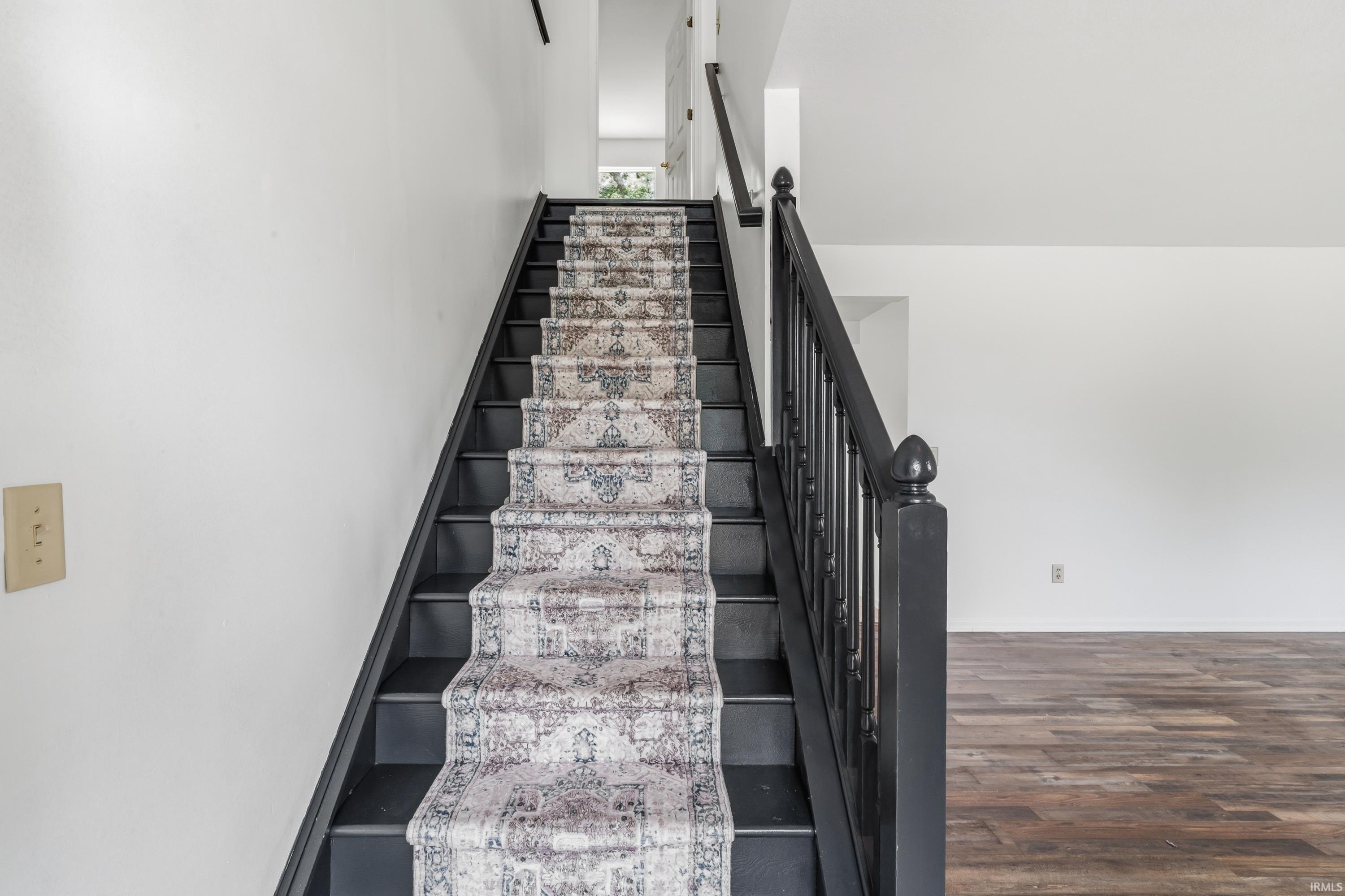 Staircase featuring dark painted treads and balusters, a patterned runner, and white walls