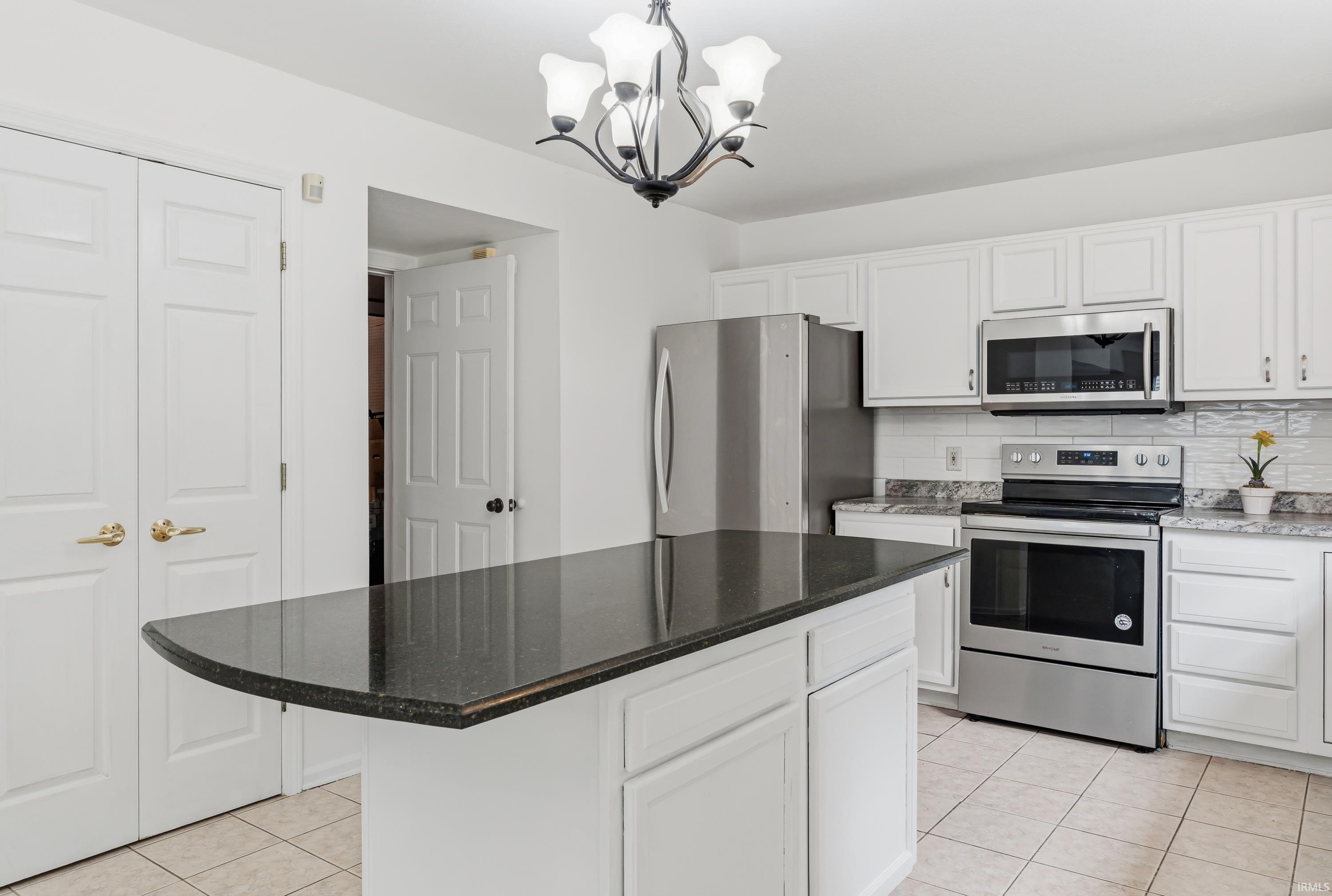 Kitchen featuring a central island with a dark countertop, white cabinetry, stainless steel appliances, and a tiled backsplash