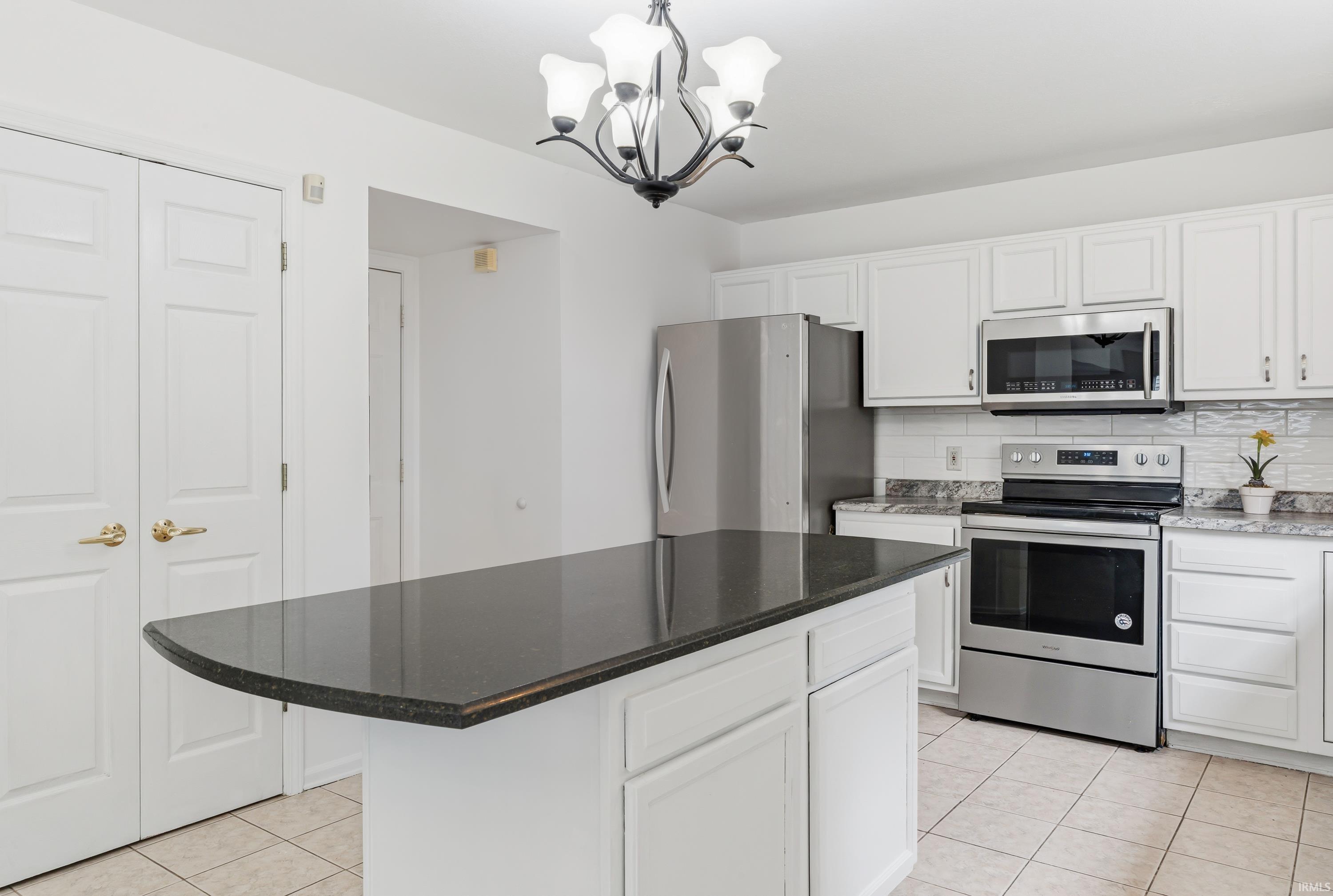 Kitchen featuring a dark countertop island, white cabinetry, stainless steel appliances, and tiled flooring