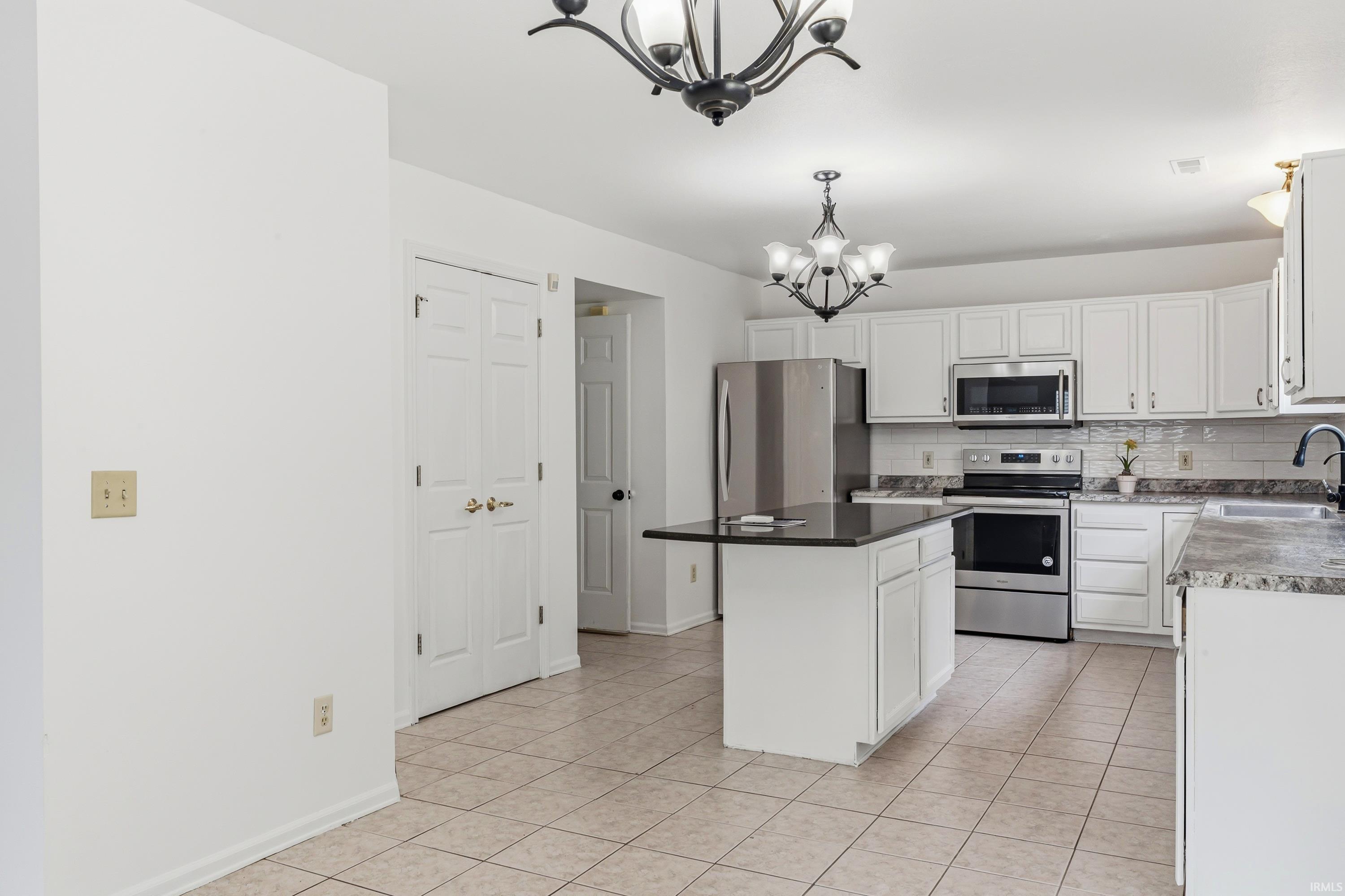 Kitchen featuring white cabinetry, stainless steel appliances, a center island with a dark countertop, and tile flooring