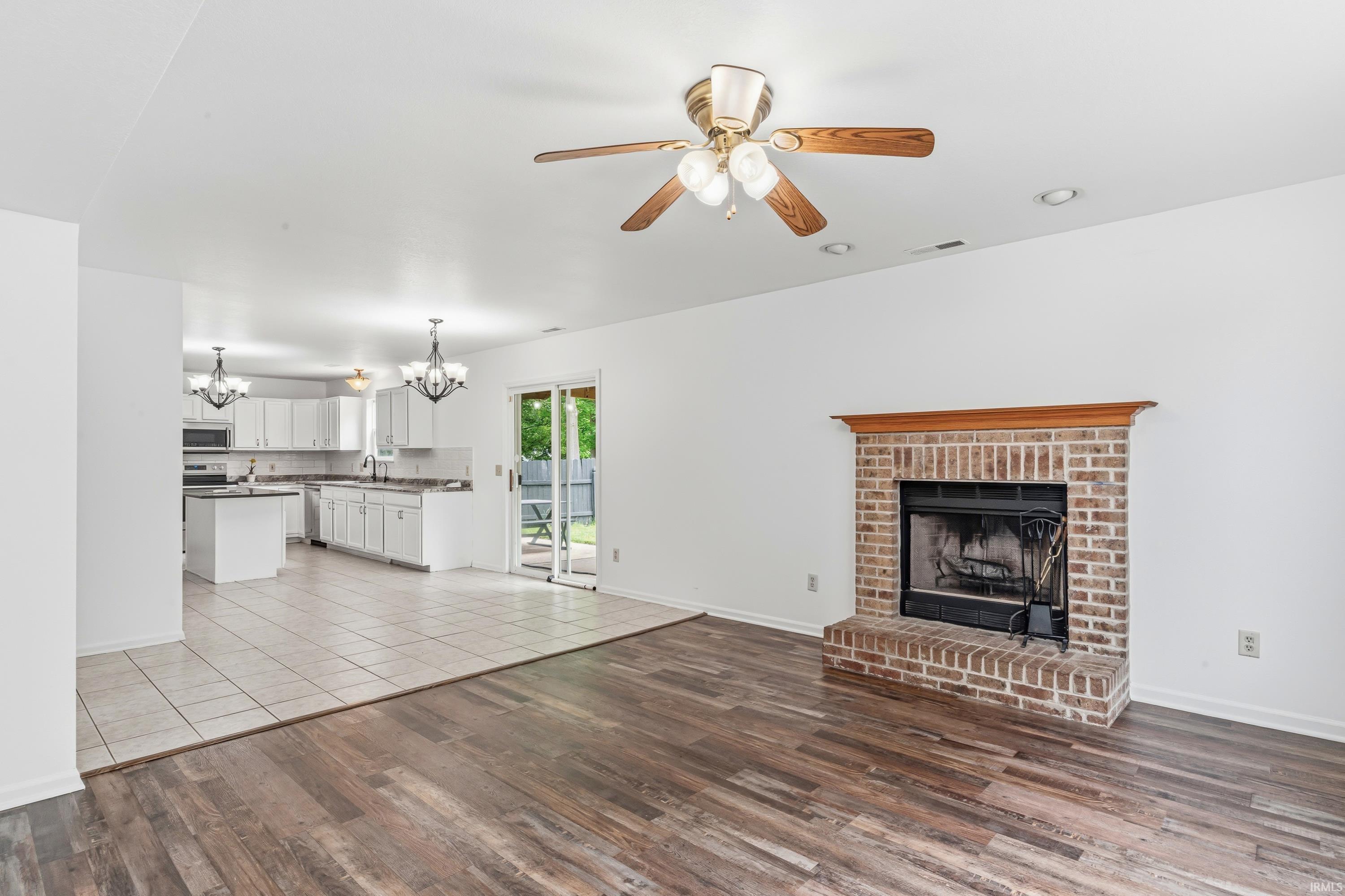 Living area featuring a brick fireplace with a wood mantel, wood-finish flooring, and a ceiling fan