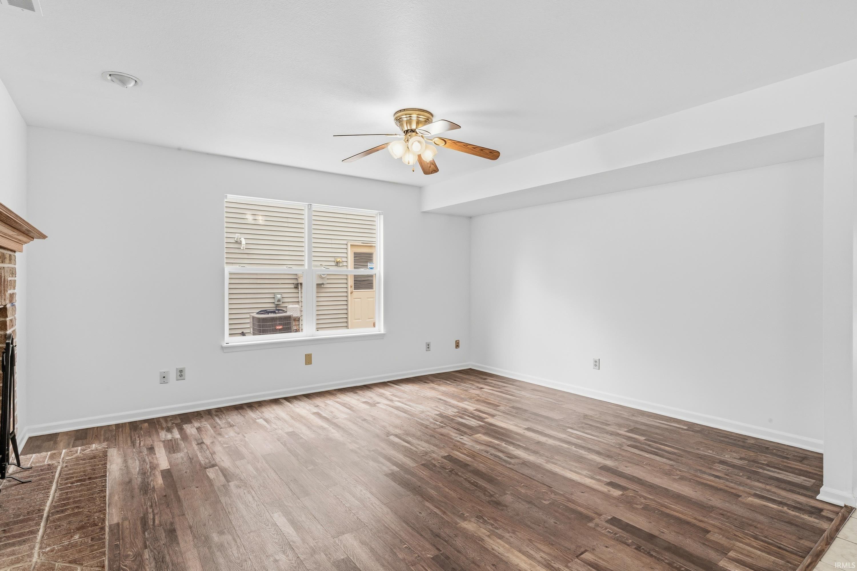 Spacious room featuring wood-finish flooring, a ceiling fan with integrated lighting, and a window with horizontal blinds