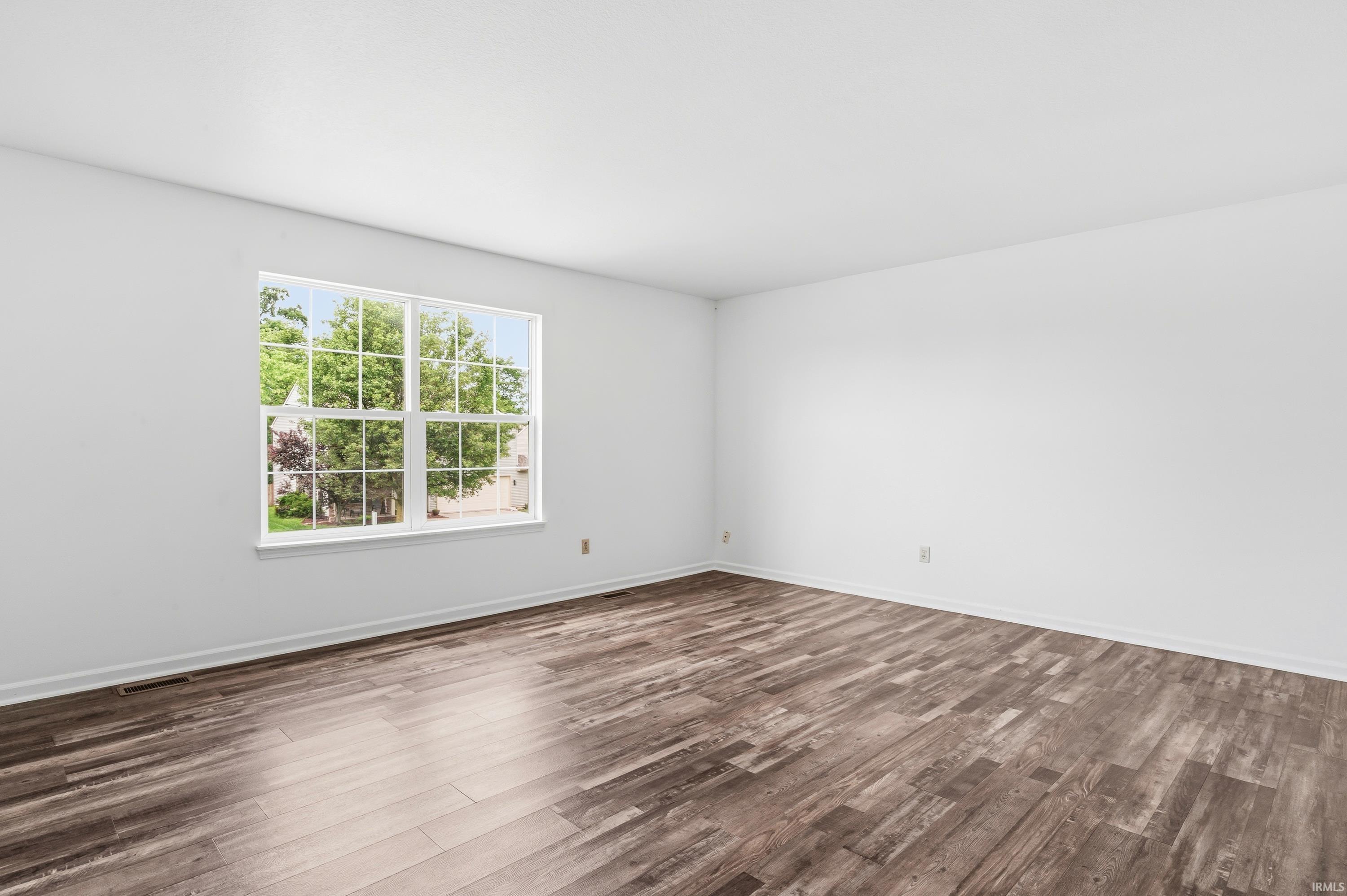 Spacious room featuring wood-finish flooring, crisp white walls, and a large window with white muntins and trim