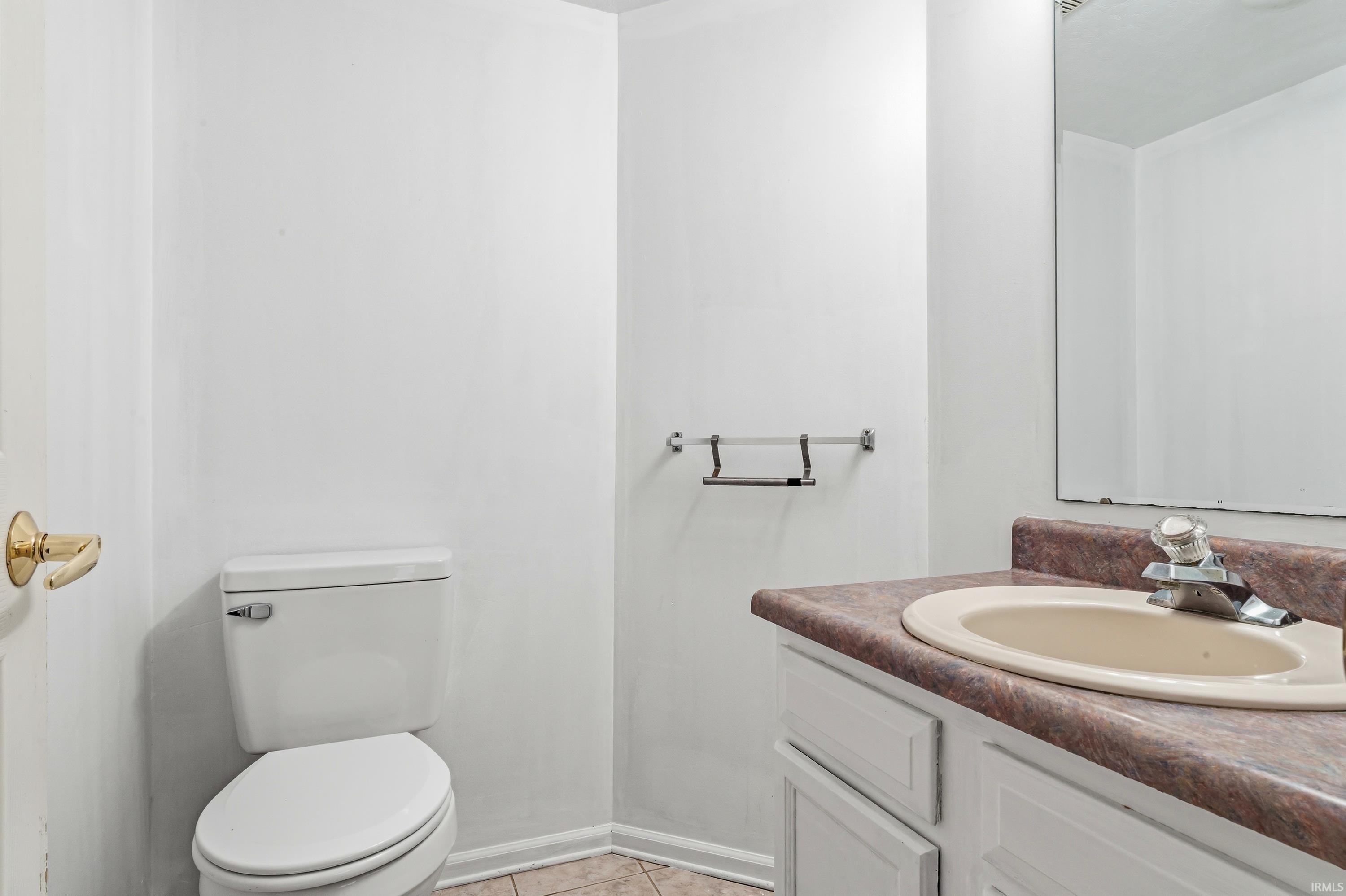 Bathroom featuring a white toilet, light-colored tile flooring, a vanity with a laminate countertop, and a wall-mounted mirror