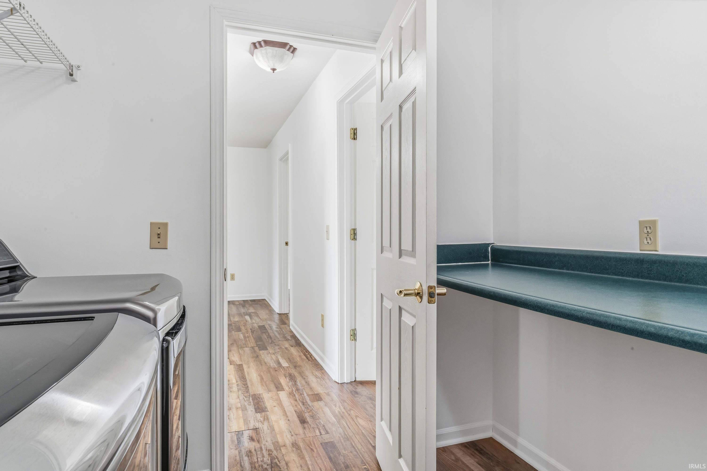 Laundry area featuring a built-in counter, wire shelving, and wood-finish flooring extending into the hallway