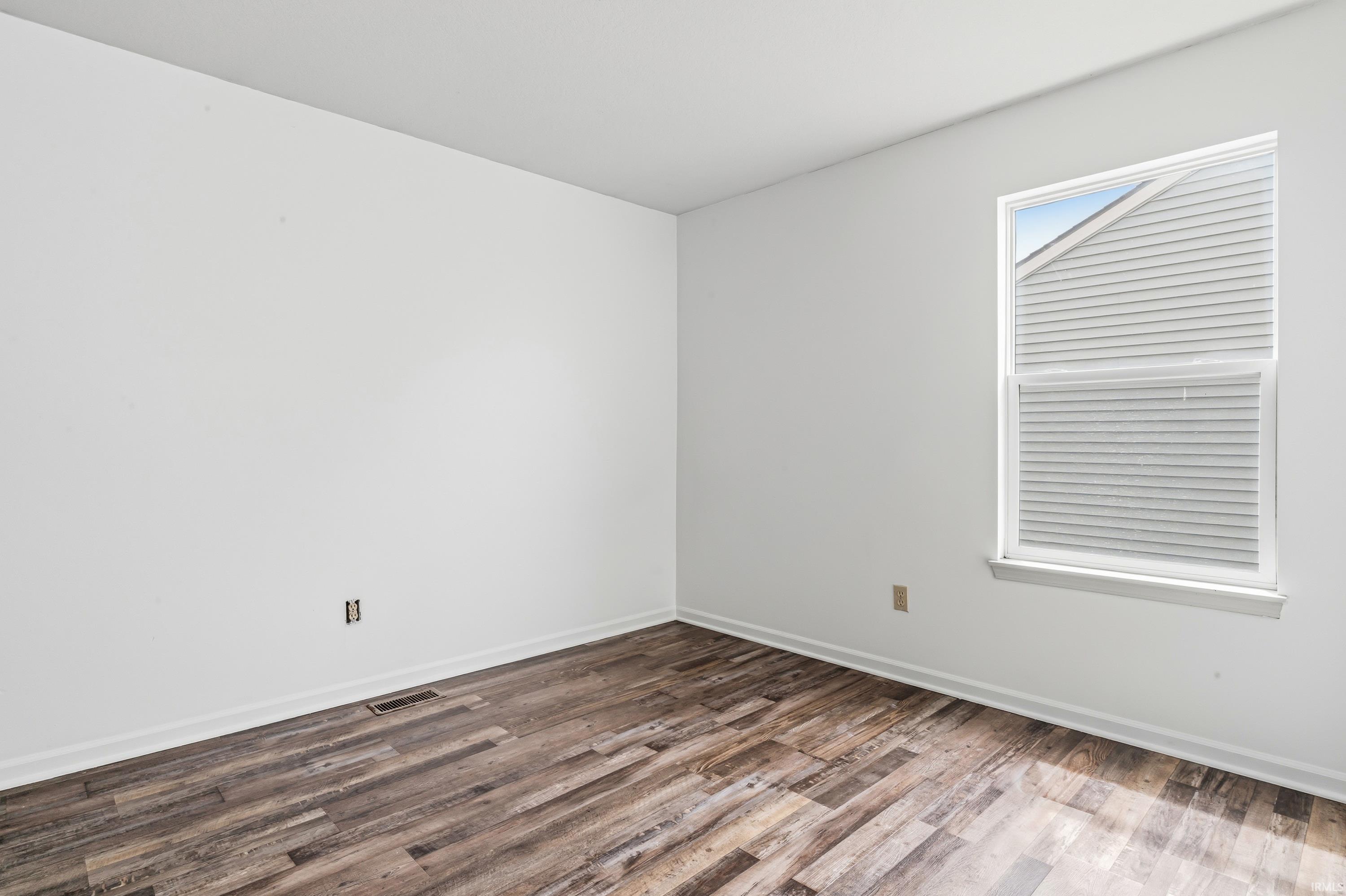 Room featuring wood-finish flooring, white walls, and a window with blinds