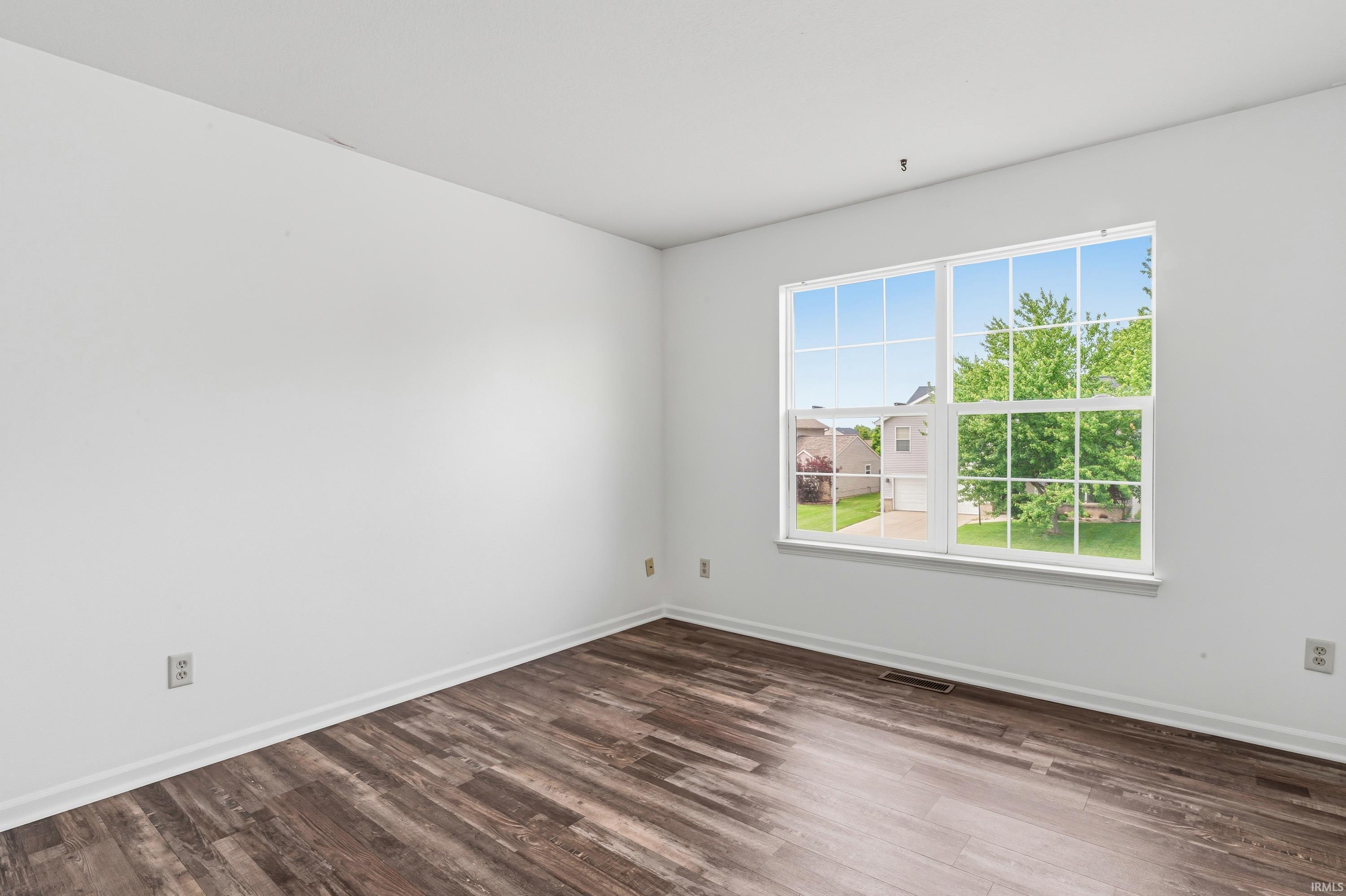 Room featuring wood-finish flooring, white baseboards, and a large window with white muntins