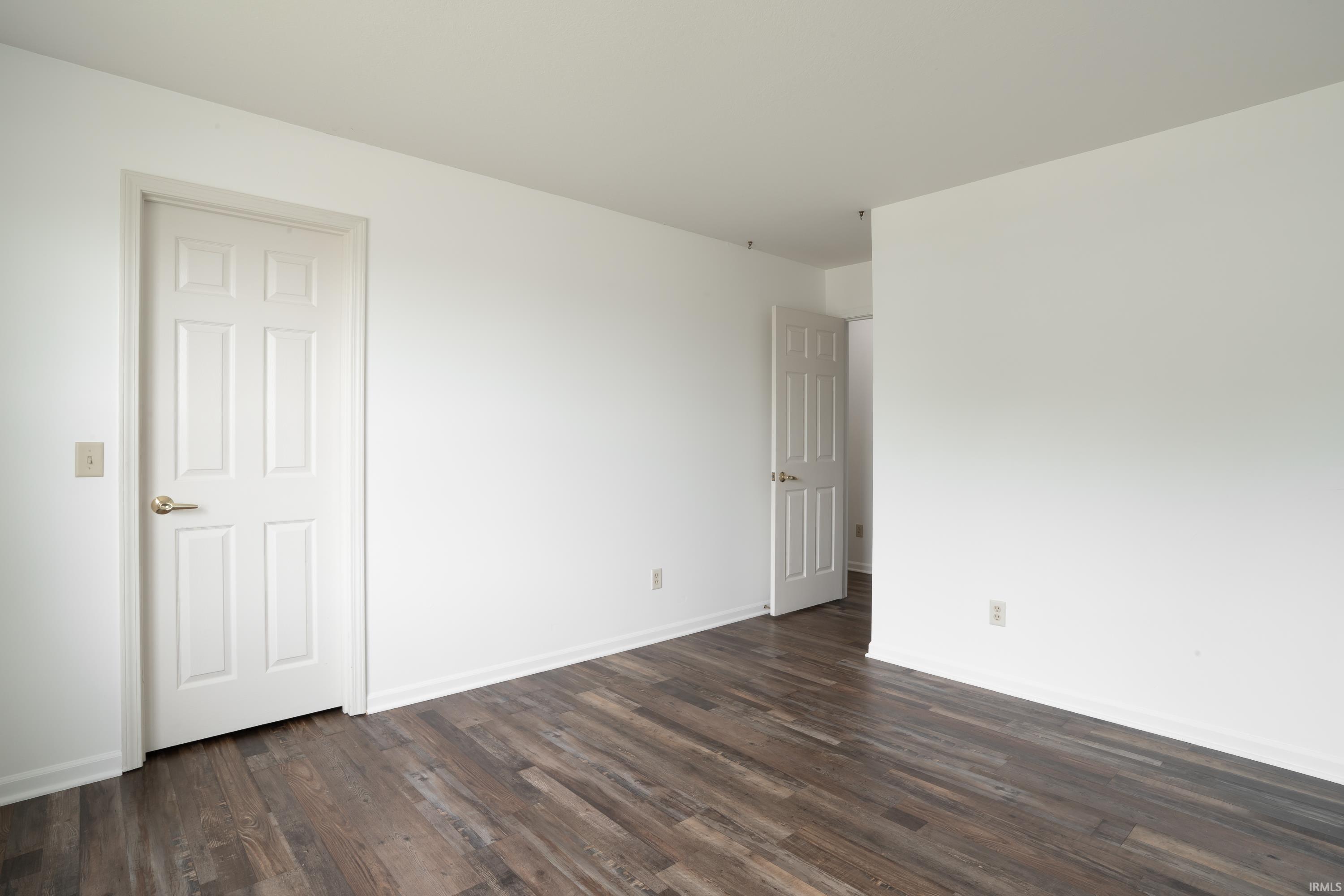 Neutral white walls and ceiling, dark wood-finish flooring, white baseboards, and white six-panel doors