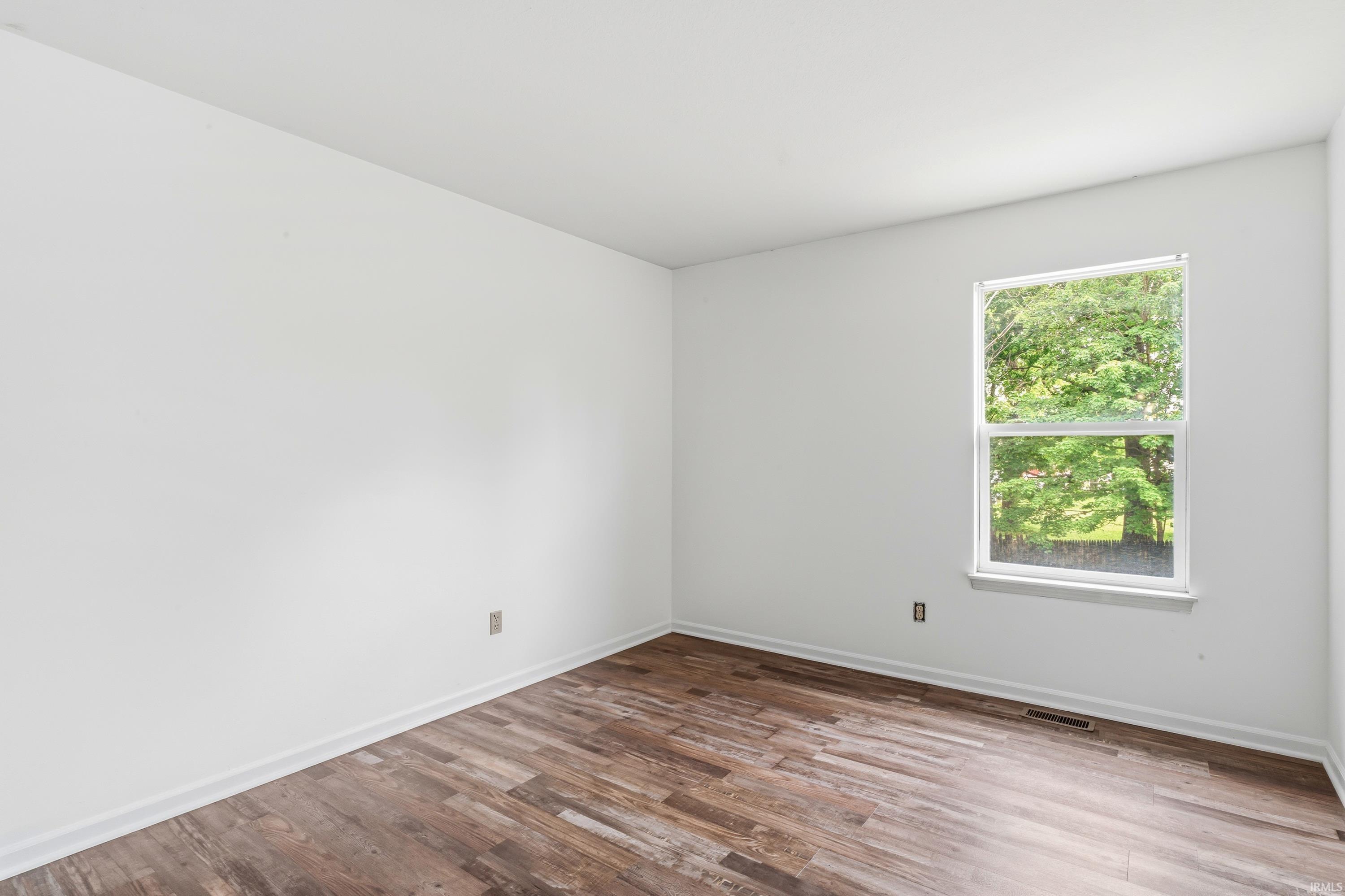 Bright room featuring wood-finish flooring, white walls, and a single window with white trim