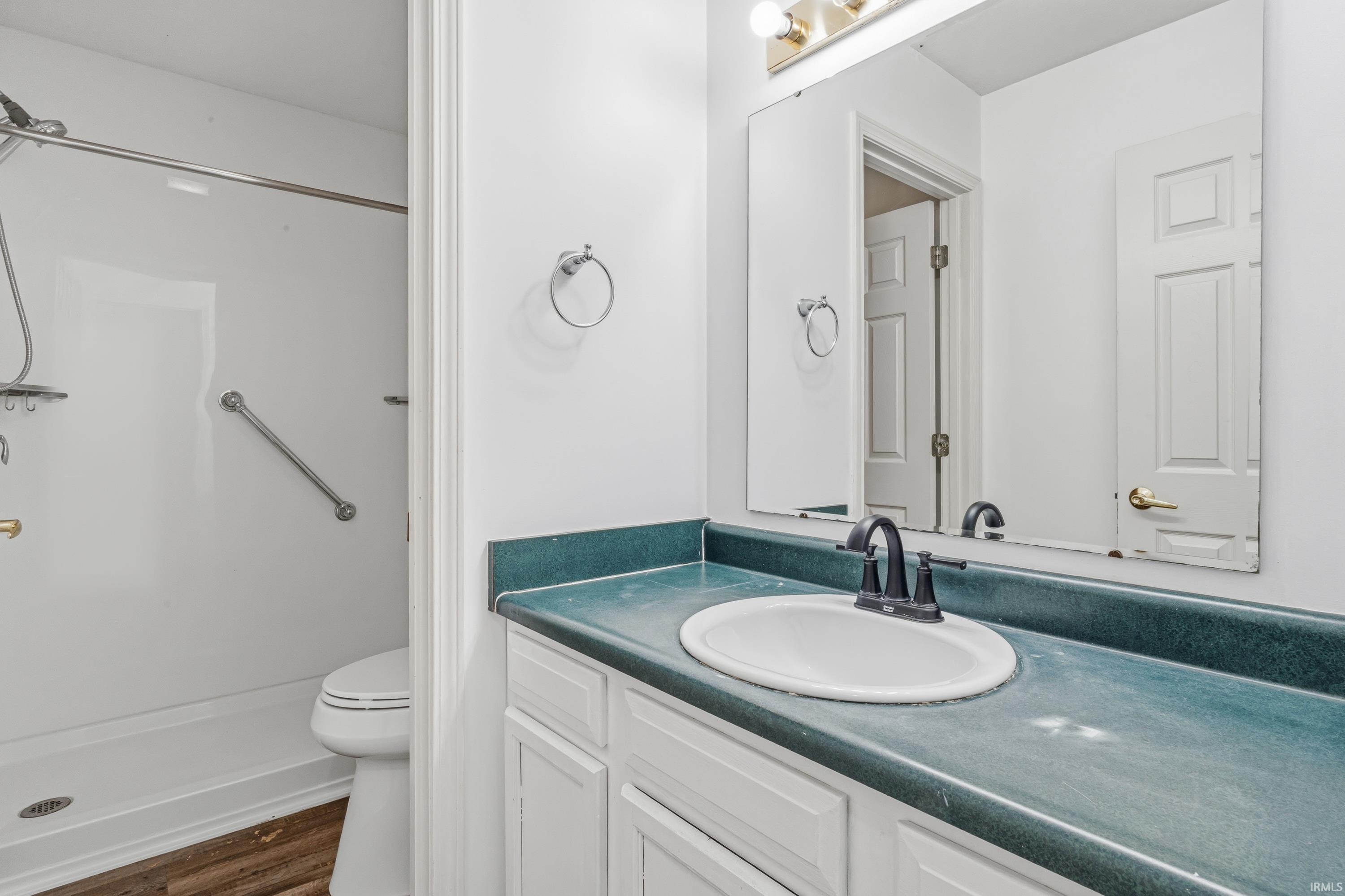 Bathroom featuring a white vanity with cabinet storage, a contrasting green countertop, an integrated sink with a matte black faucet, and a large wall-mounted mirror