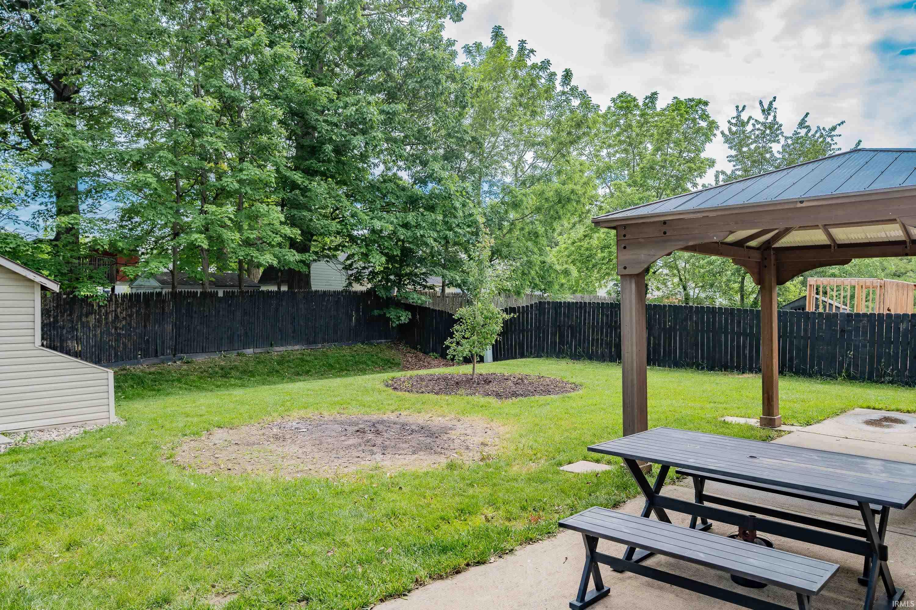 Expansive backyard featuring a gazebo with a dark metal roof, a concrete patio, and a manicured lawn