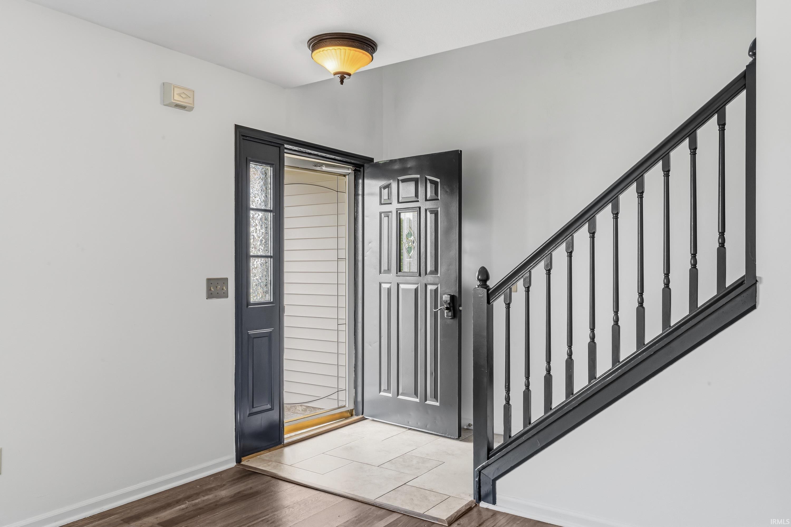 Entryway featuring a dark paneled door with decorative glass, tile flooring, and a coordinating dark wood-finish staircase with balusters