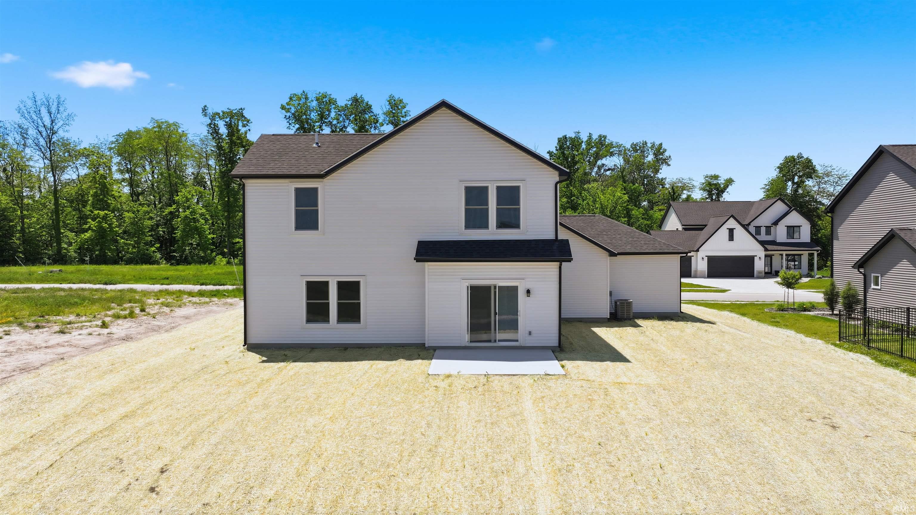Rear elevation featuring white siding, a dark shingle roof, and a sliding glass door opening to a concrete patio