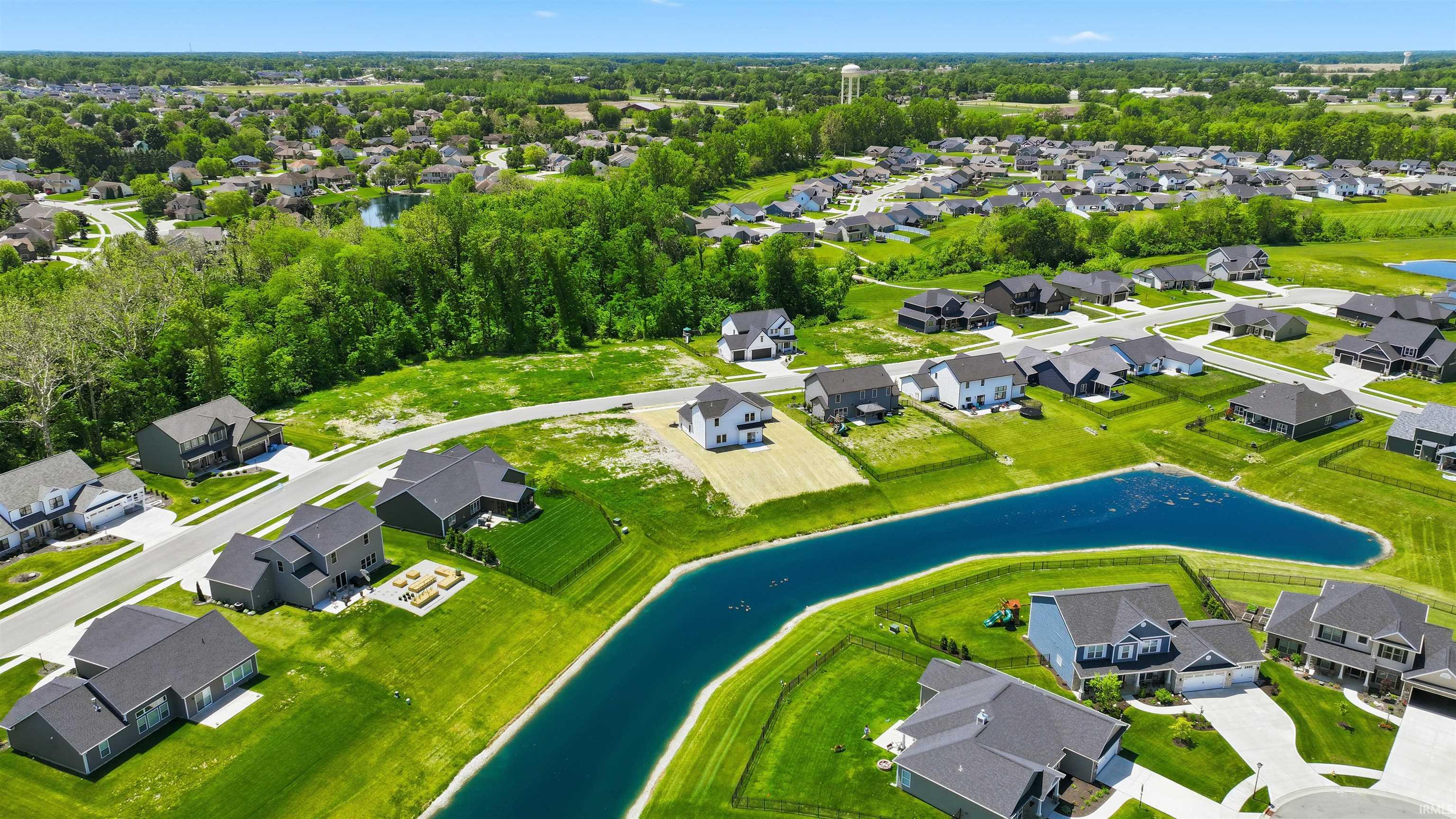 Aerial overview of a residential development featuring newly constructed homes, established landscaping, and a central pond