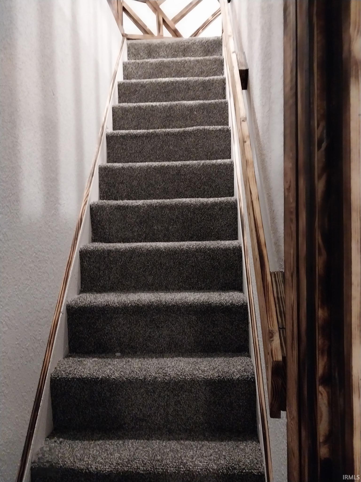 Staircase featuring grey carpeted treads, white risers, and a natural wood handrail