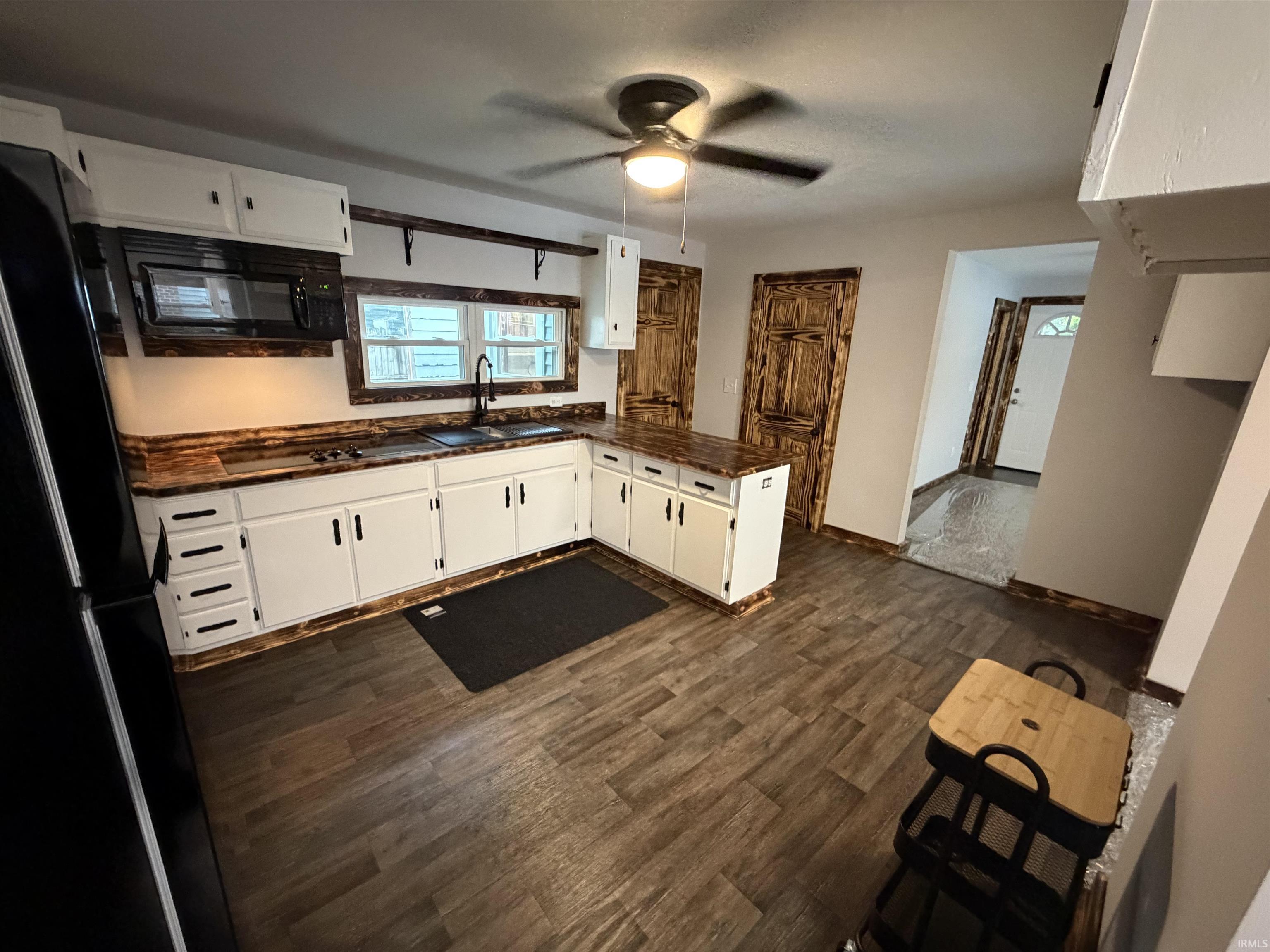Kitchen featuring L-shaped countertop with integrated sink, white cabinetry, dark wood-finish flooring, and a ceiling fan with integrated lighting