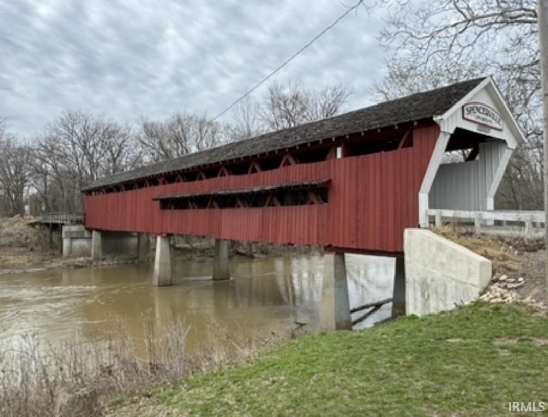 Red covered bridge spanning a waterway, featuring a white gabled entrance with signage