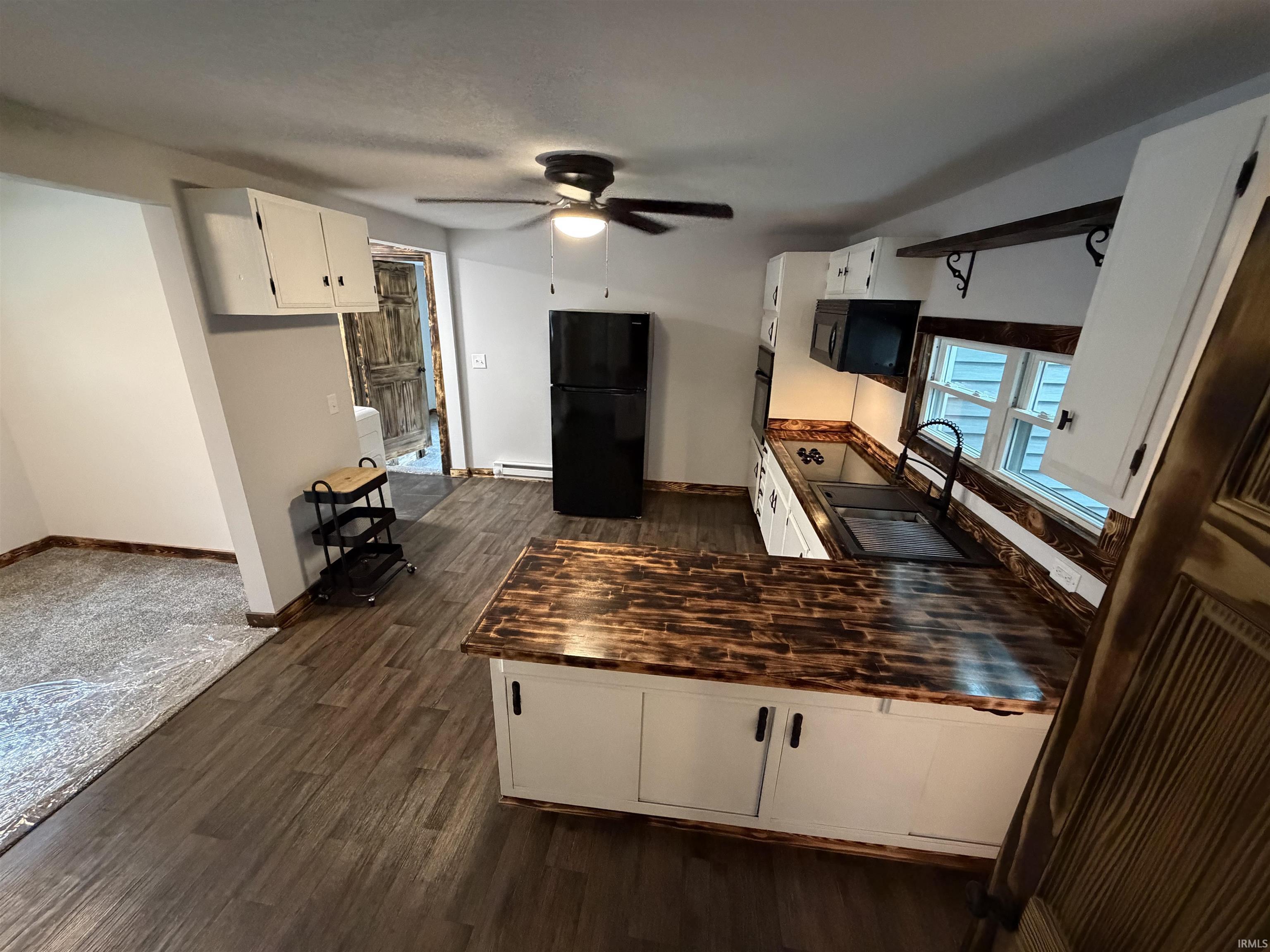 Kitchen featuring wood-finish flooring, white cabinetry, dark wood countertops, a double basin sink with a gooseneck faucet, and a black refrigerator
