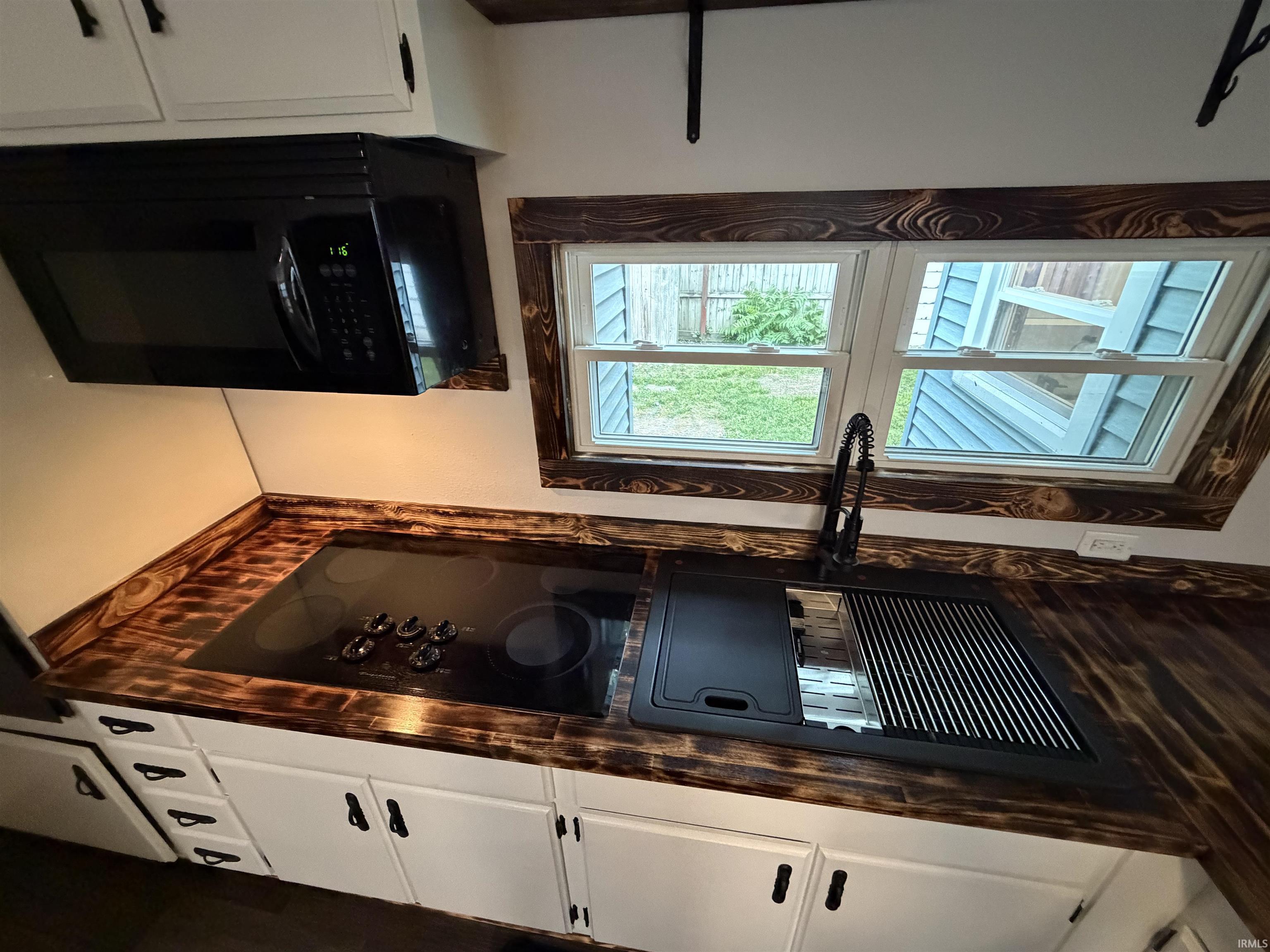 Kitchen featuring burnished wood-finish countertops, white cabinetry with dark hardware, a built-in black cooktop, an under-cabinet microwave, and a black gooseneck faucet